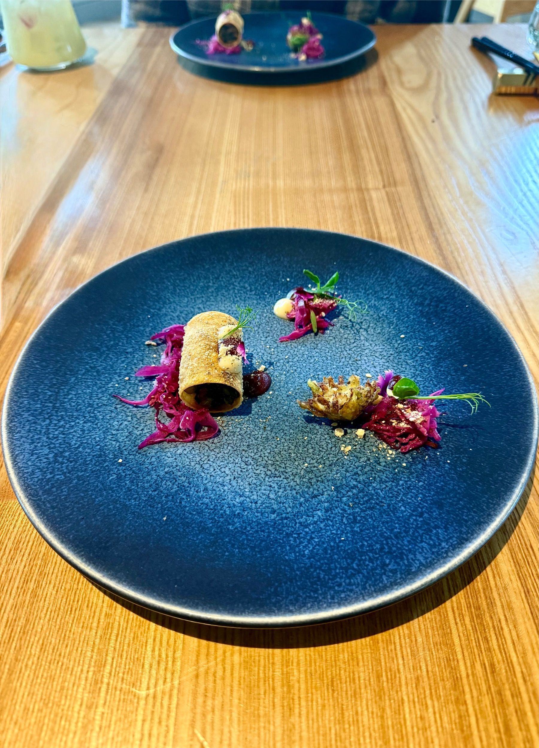 Charred cabbage with delicate garnish plated on a deep blue ceramic dish.
