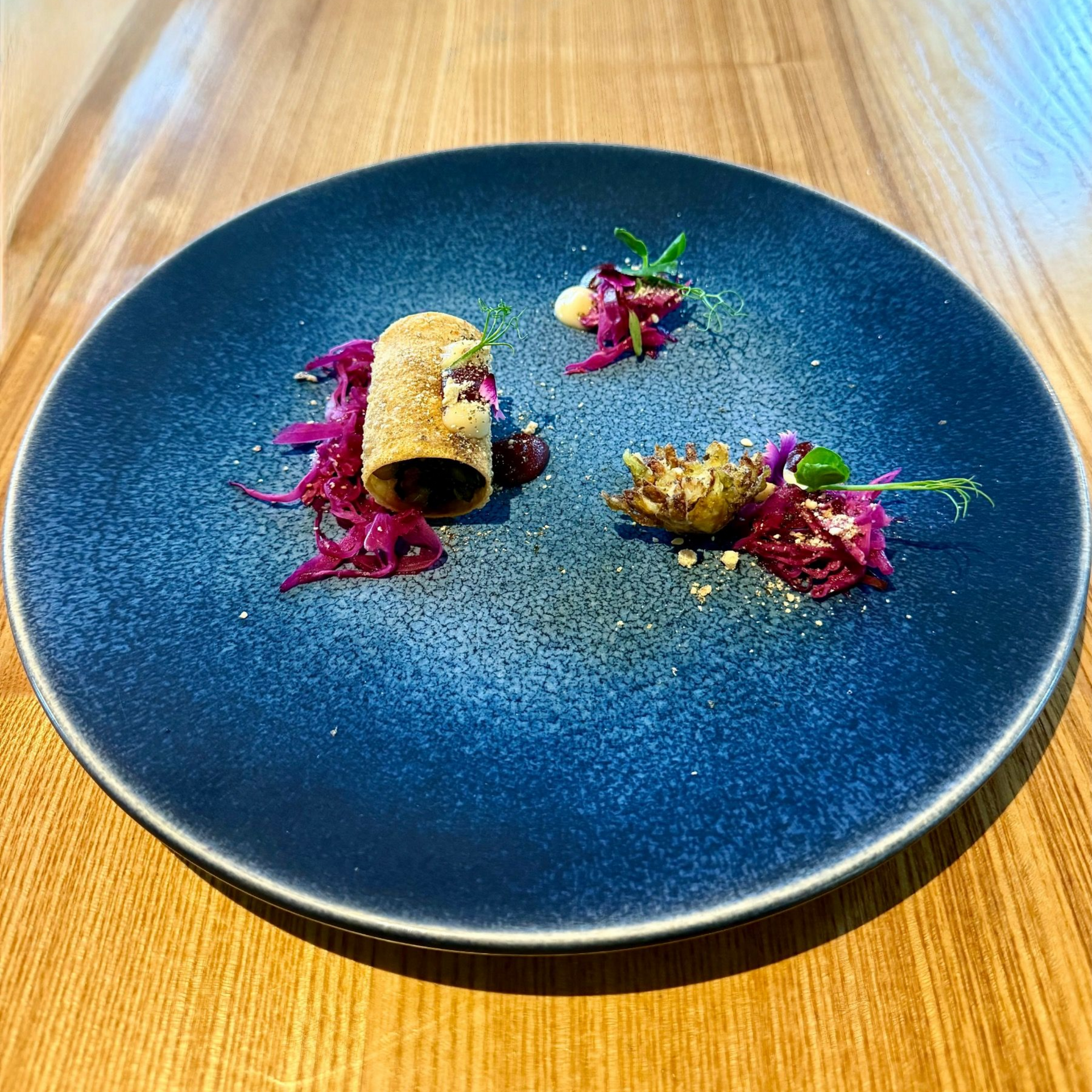Charred cabbage with delicate garnish plated on a deep blue ceramic dish.
