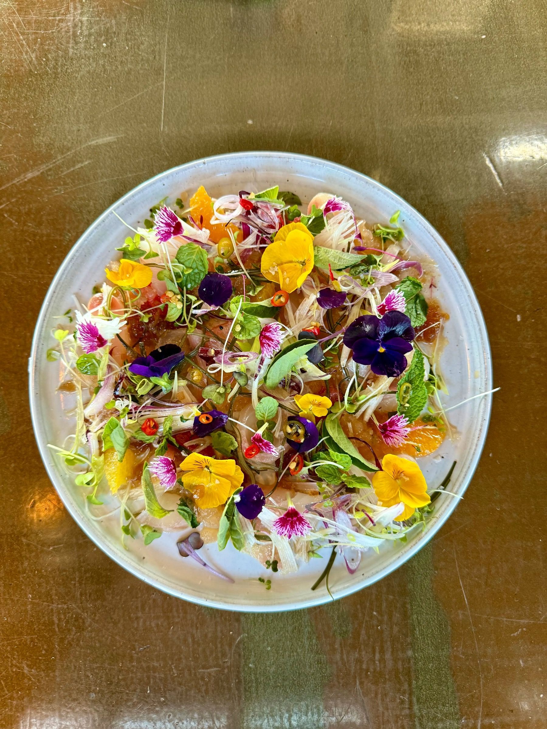 Pot Luck Club fish ceviche with citrus dressing and edible flowers on a white plate
