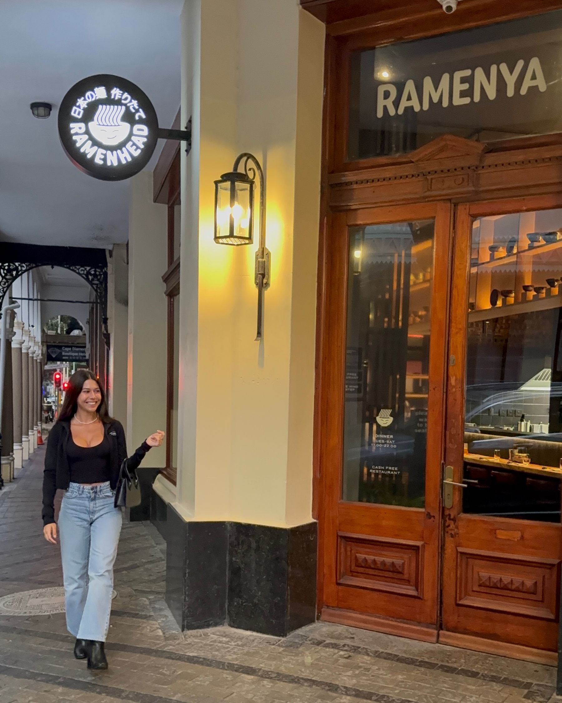Paige is standing outside the Ramenhead Cape Town entrance at night
