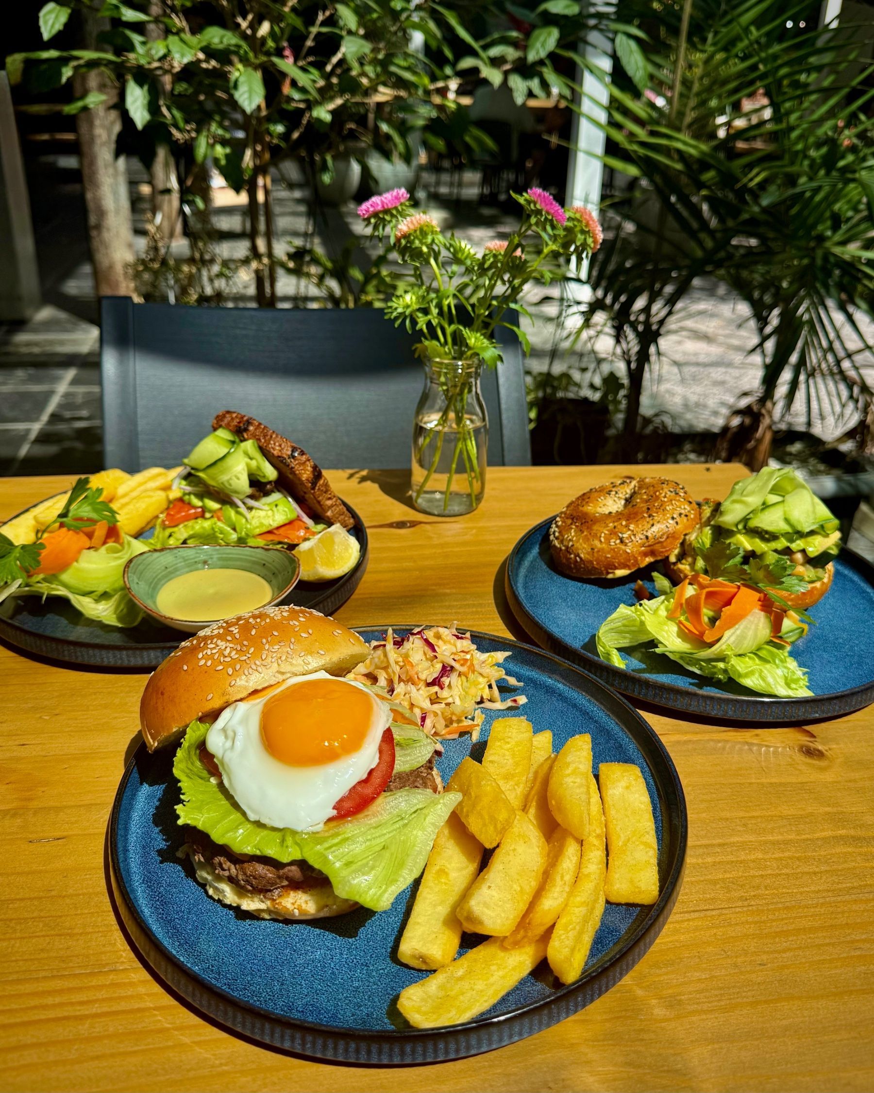 Yumcious café table spread with smoked salmon sandwich, garbanzo bagel sandwich and beef burger with fried egg and chips