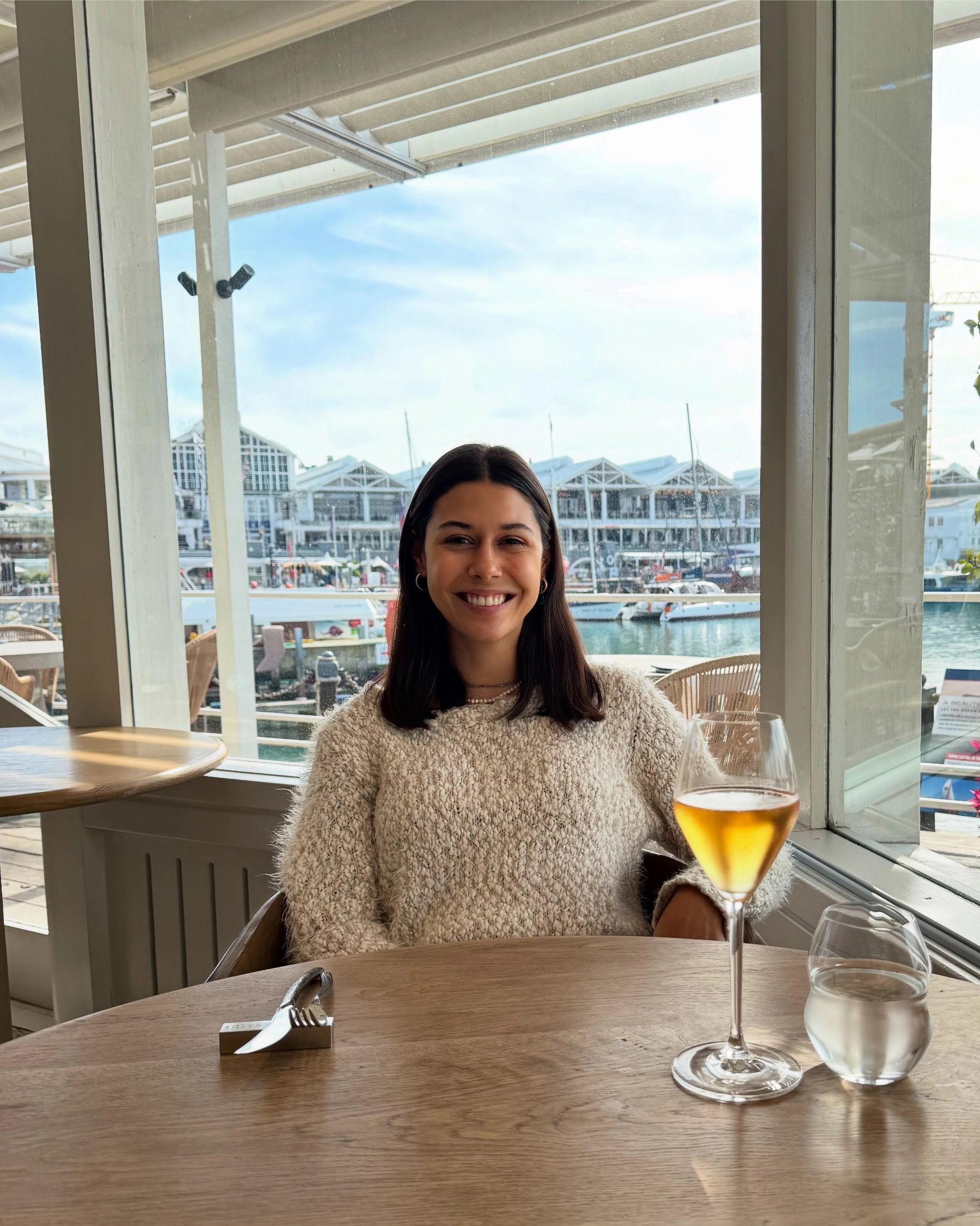 Paige seated at The Waterside in Cape Town with harbour views and a glass of rosé MCC on the table.
