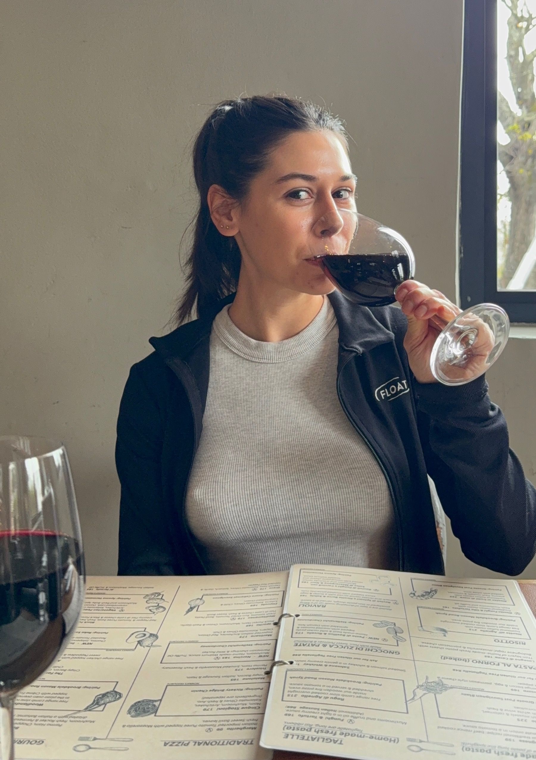 Paige holding a glass of red wine and looking toward the camera at Woodlands Eatery, Cape Town