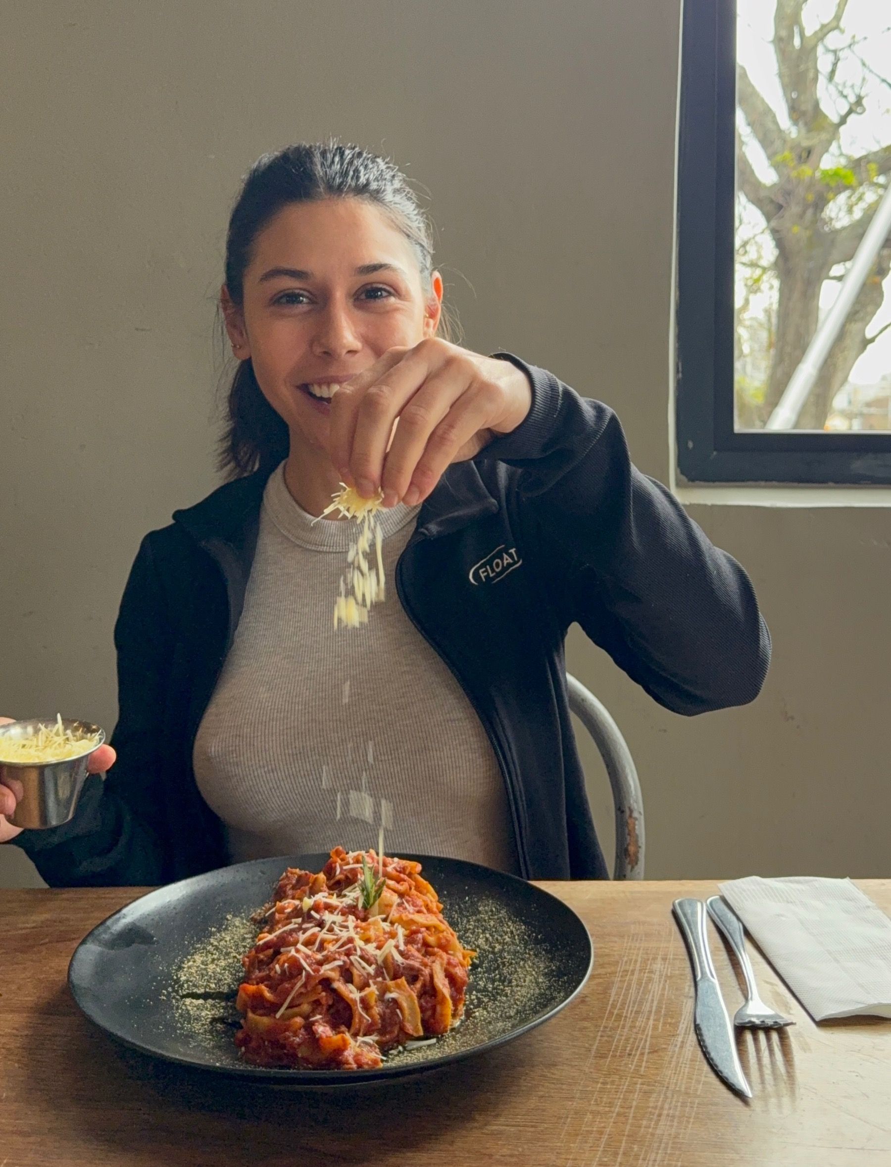 Paige sprinkling grated cheese over a bowl of pasta at Woodlands Eatery, Cape Town