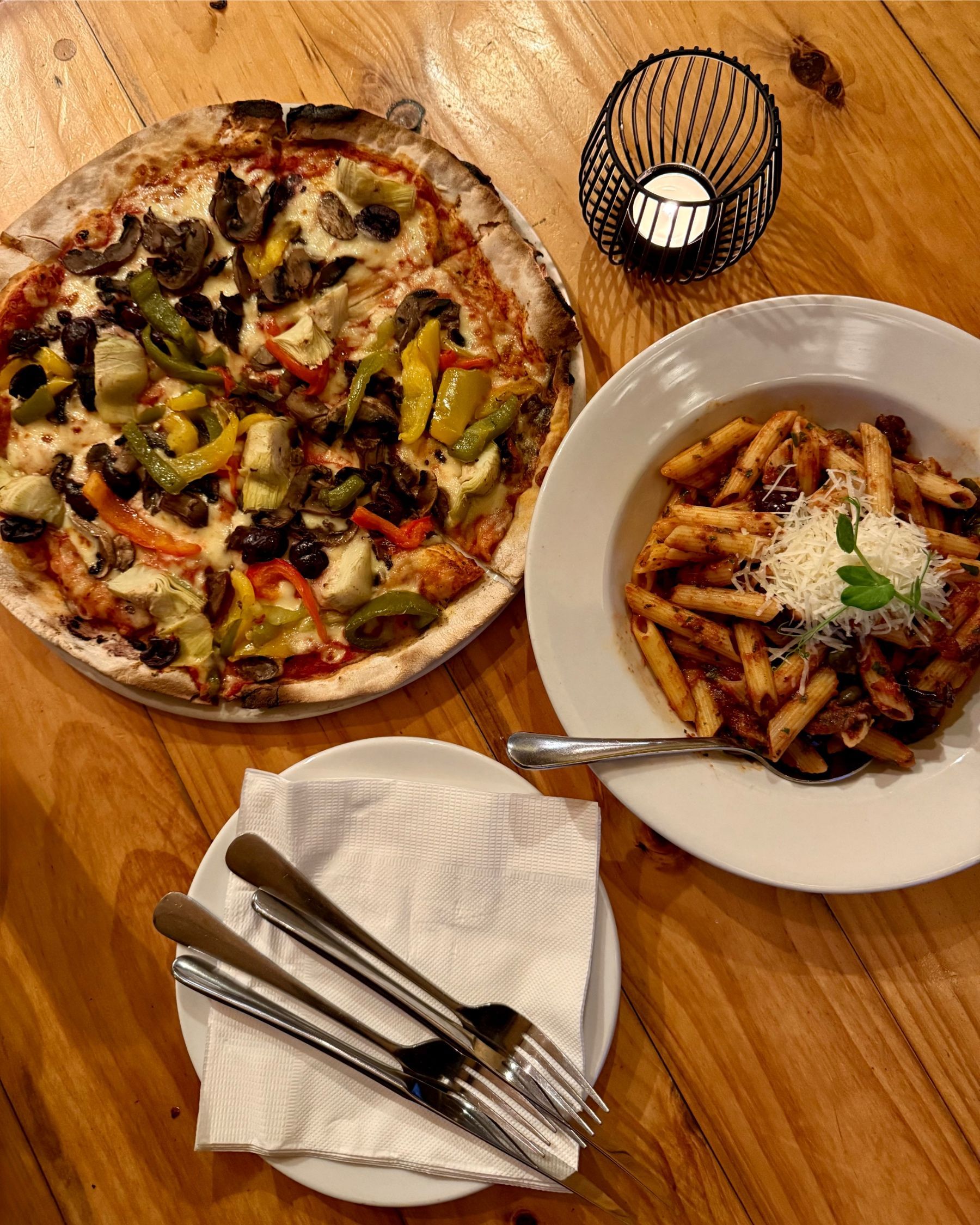 Vegetarian pizza and penne puttanesca served on a wooden table at Massimo’s.
