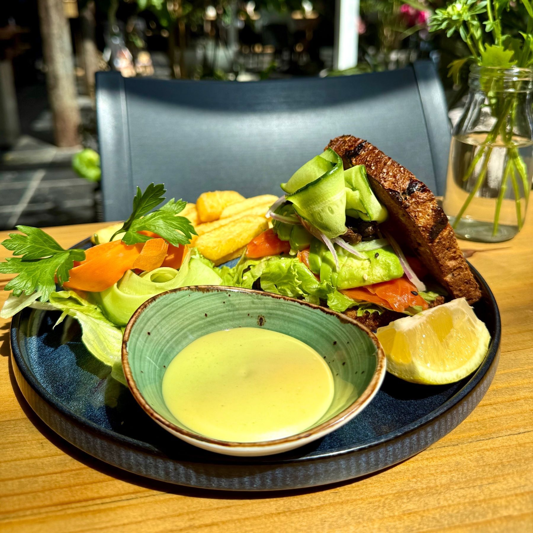Smoked salmon sandwich on toasted bread with avocado, cucumber ribbons, lettuce, served with dressing at Yumcious Café
