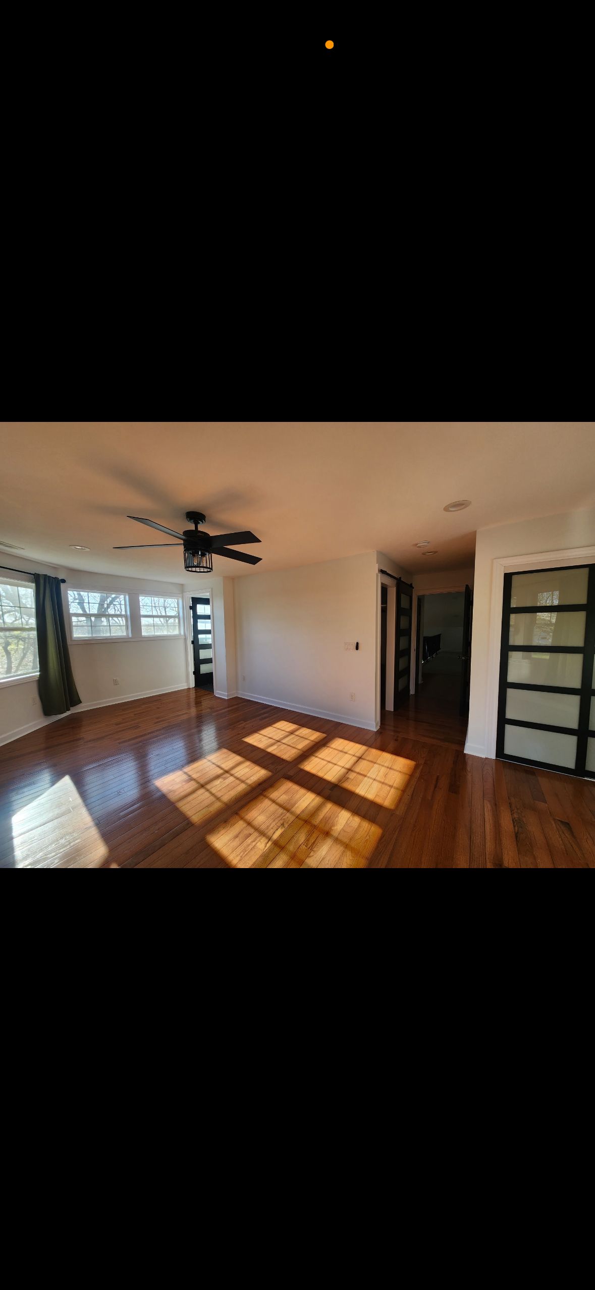 An empty living room with hardwood floors and a ceiling fan.