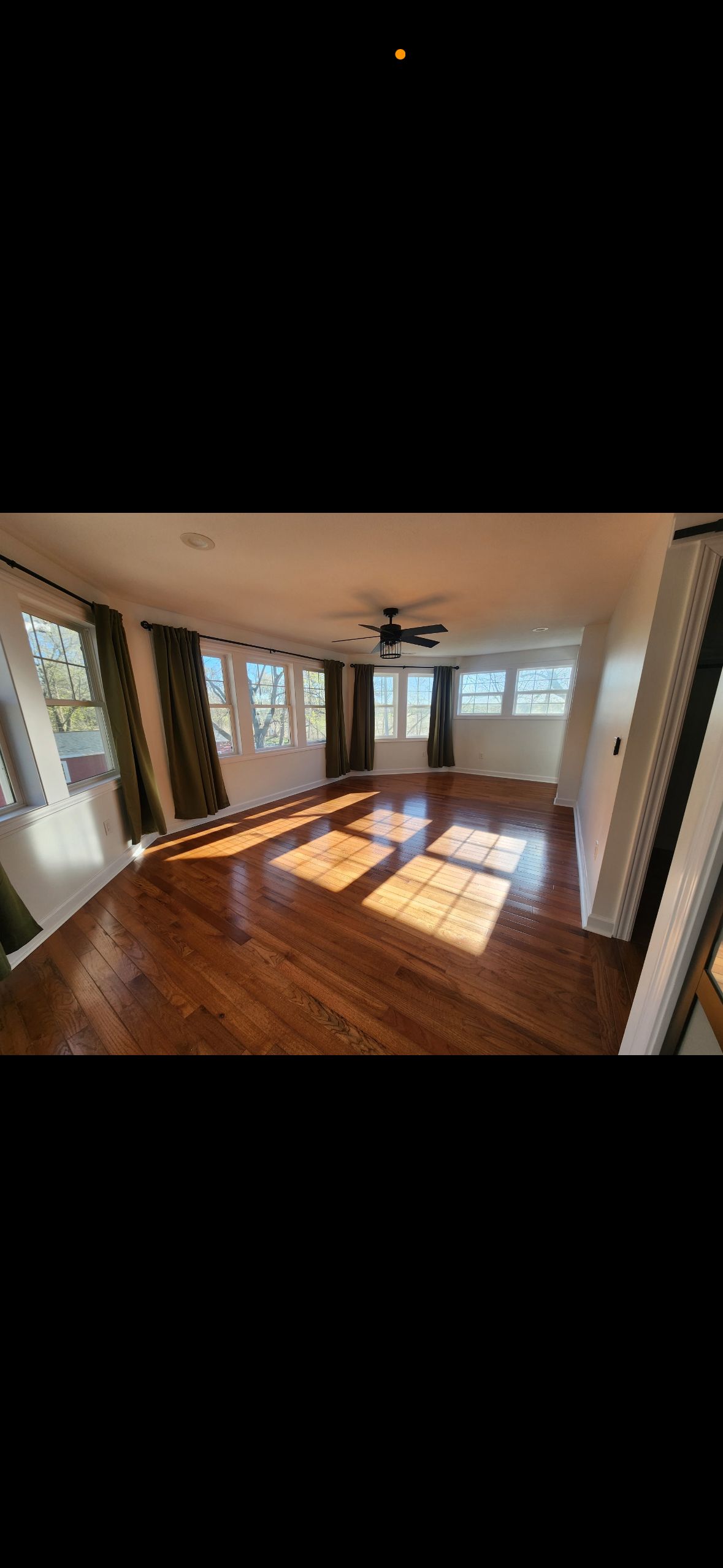 A large empty living room with hardwood floors and a ceiling fan.