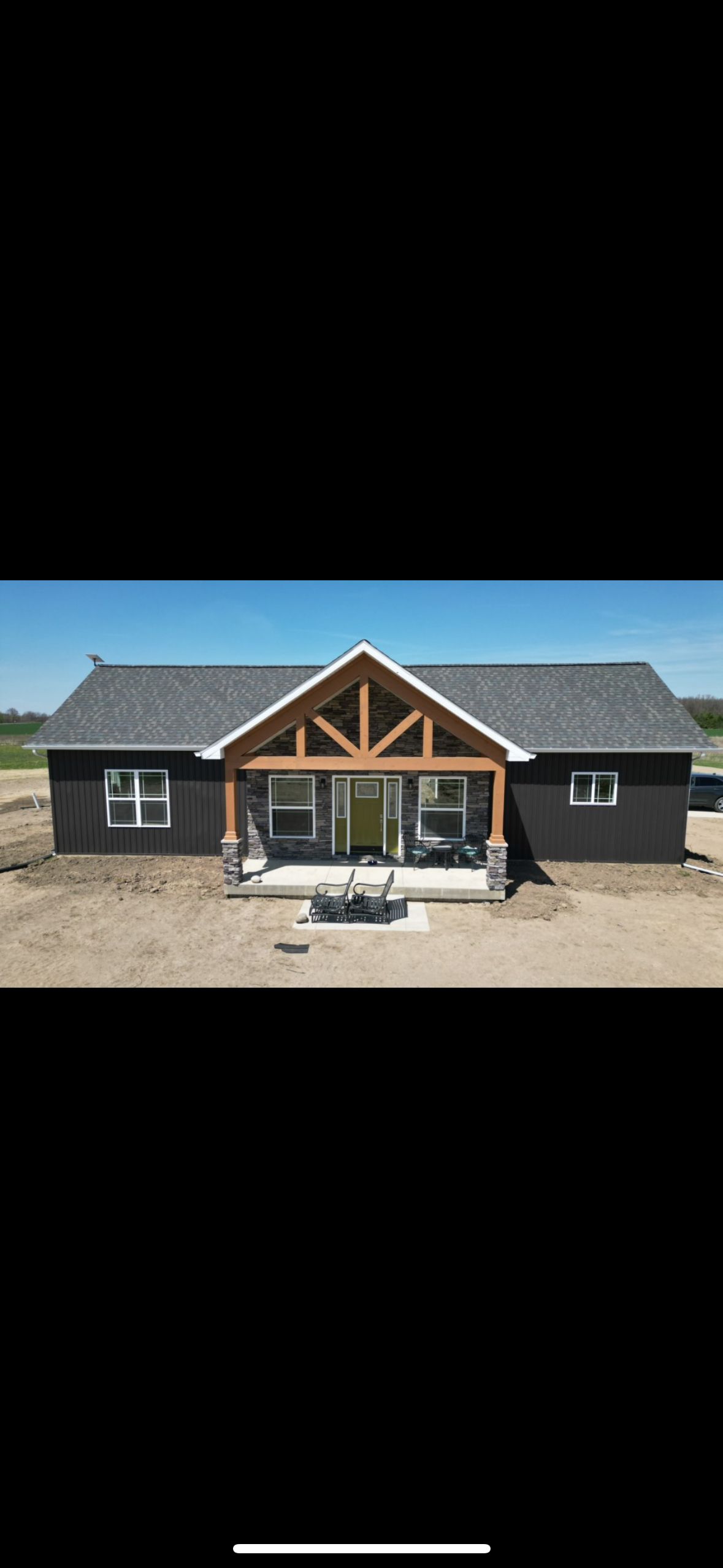 A large house with a large porch and a gray roof is sitting on top of a dirt field.