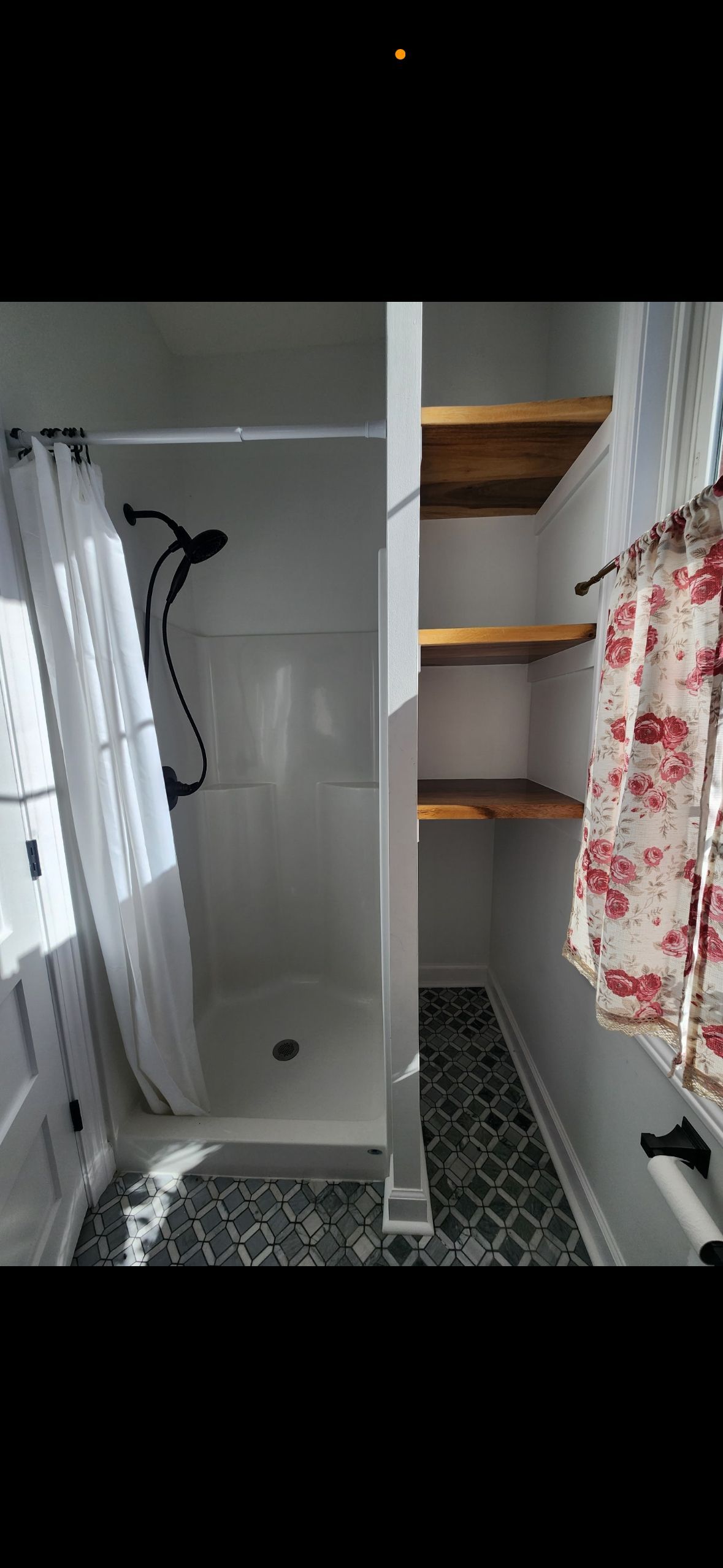 A bathroom with a shower , shelves , and a window.
