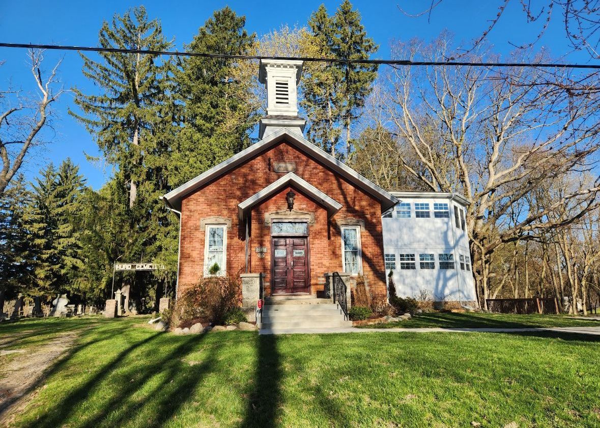 A small brick church with a steeple in the middle of a grassy field.