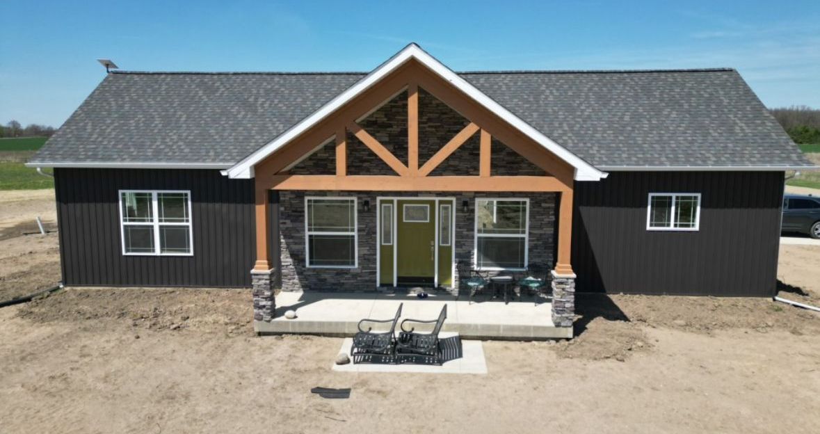 An aerial view of a house with a porch and chairs in front of it.