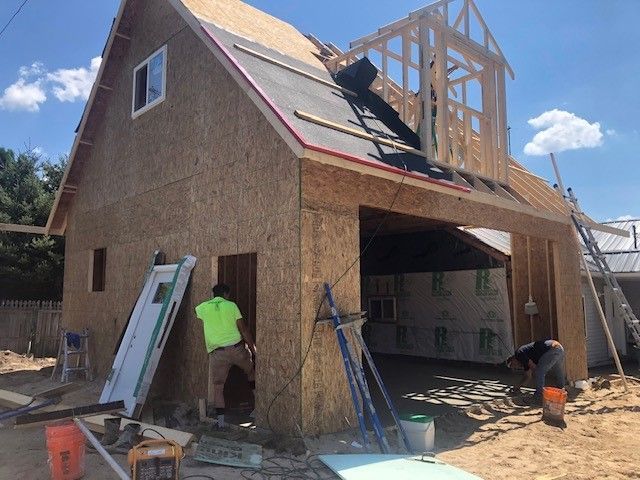 A man in a green shirt is standing in front of a house under construction.