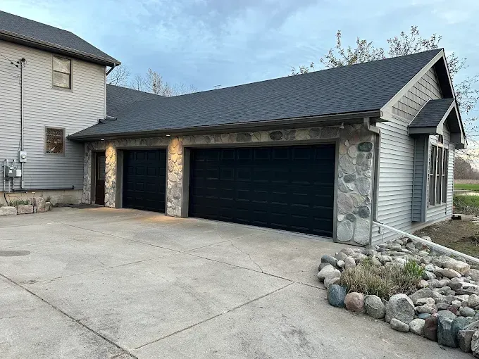 A garage with two black garage doors is next to a house.