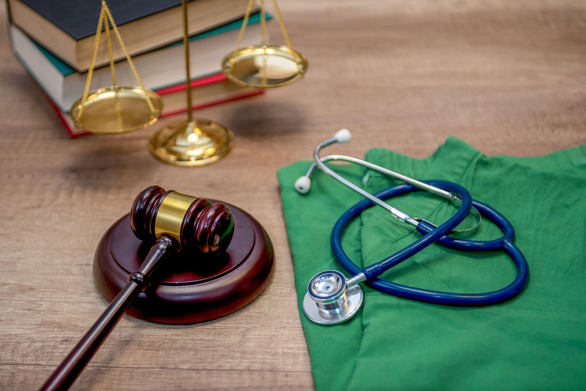 A judge 's gavel , stethoscope , scales and a green scrub on a wooden table.