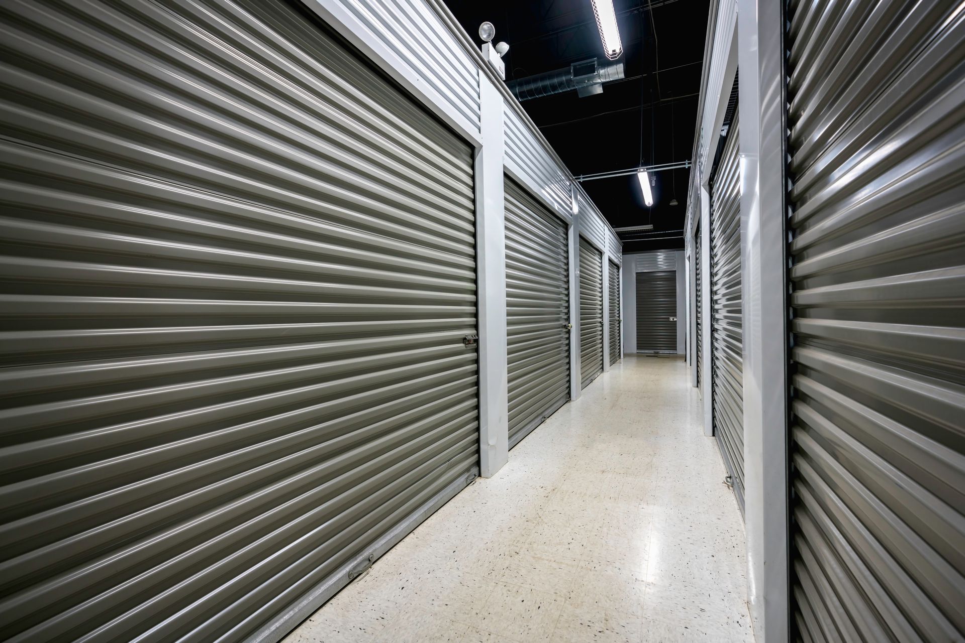 Clean hallway with secure metal roll-up doors at a modern self storage facility.