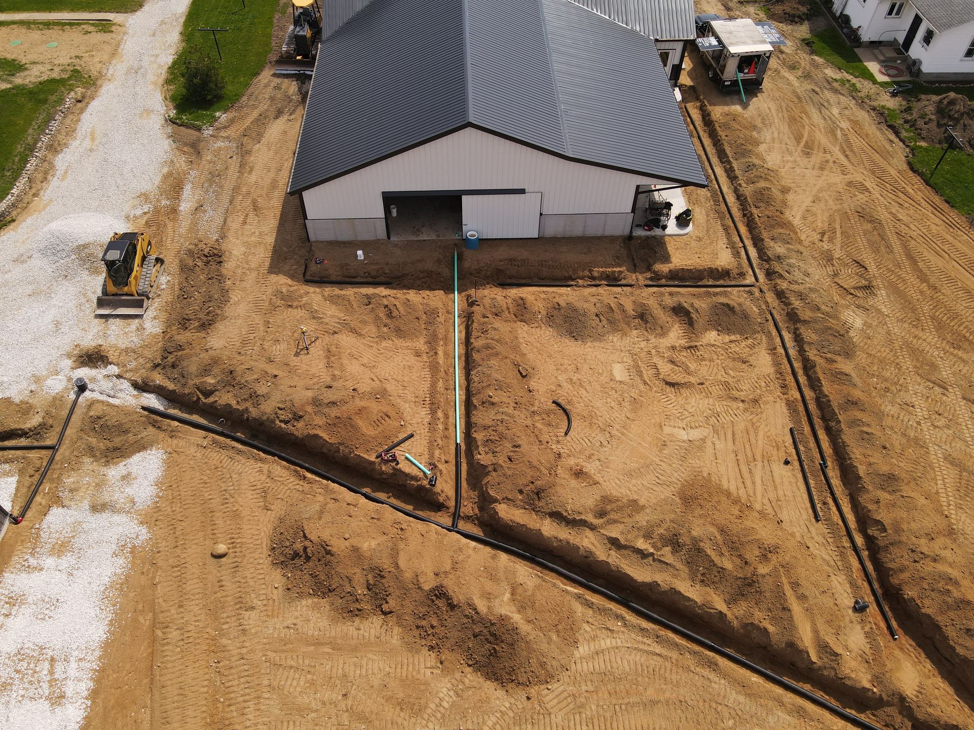 Overhead view of a new white building with a black roof and trenches dug in dirt. Construction site.