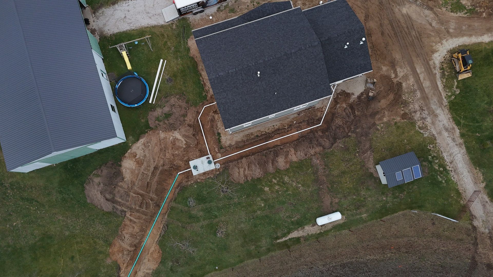 Aerial view of a house and surrounding yard with construction in progress; brown soil and grass.
