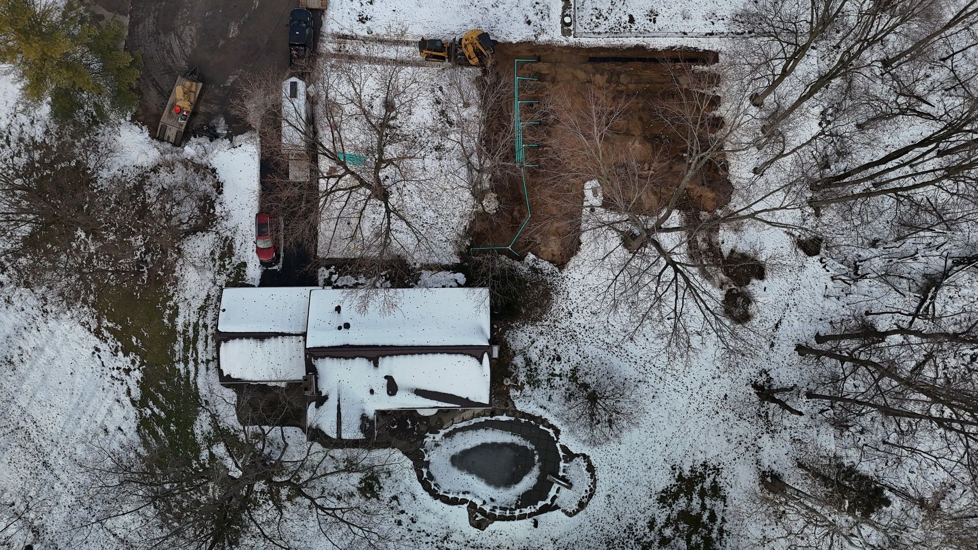 Overhead view of a snow-covered house and yard, surrounded by trees.