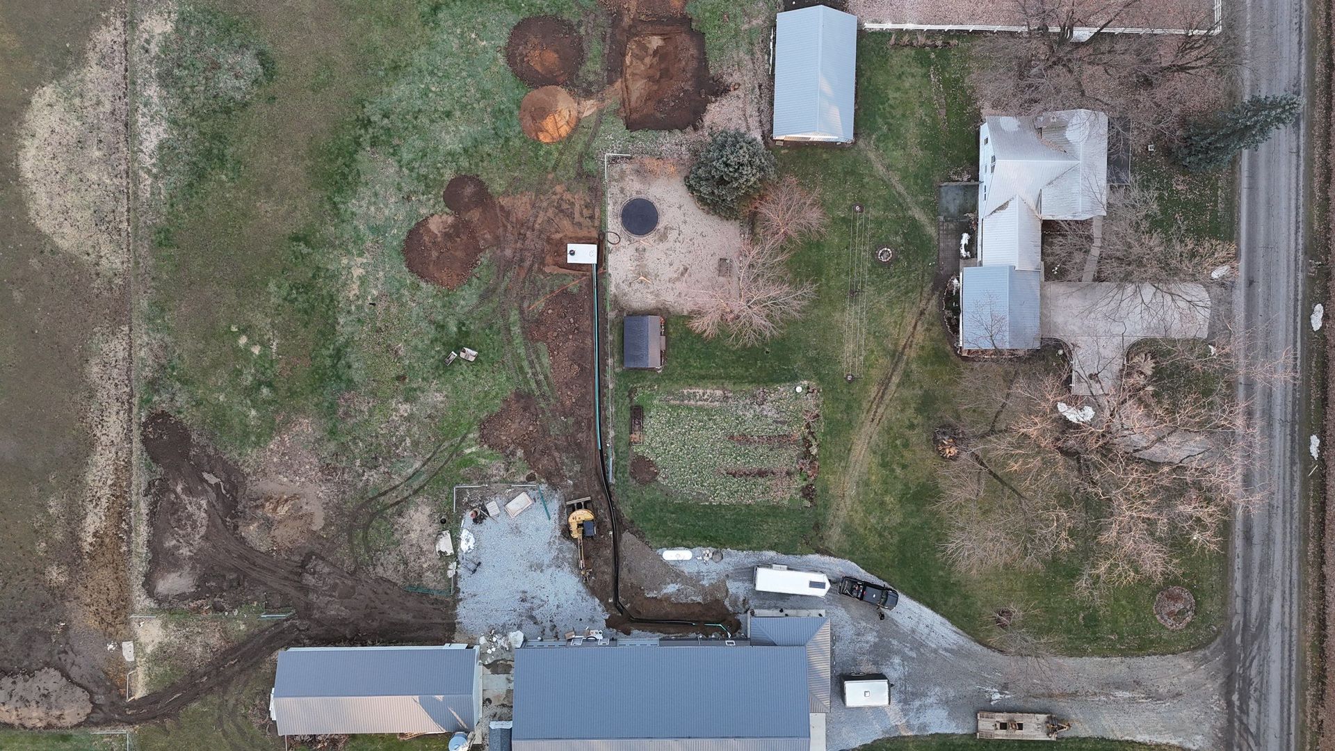 Overhead view of a rural property with buildings, driveway, and field. Brown, green, and gray tones dominate.