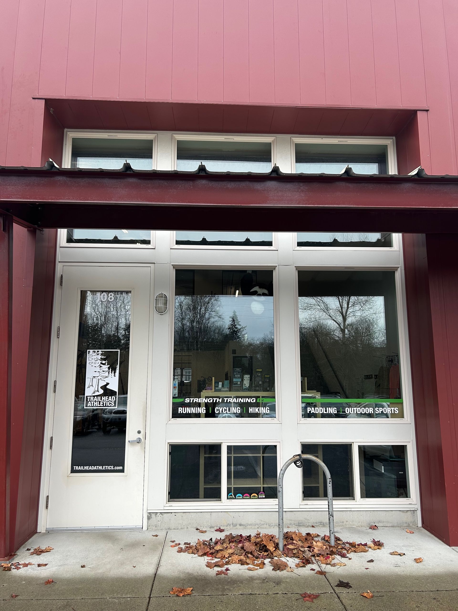 A red-walled storefront with a white-framed glass door and windows, featuring a bicycle rack on the sidewalk.