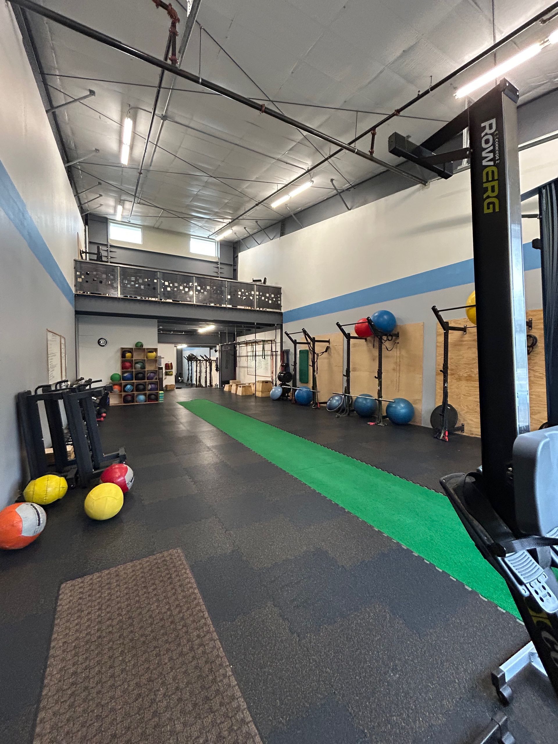 A gym interior with black rubber flooring, a long green turf strip, fitness equipment, wall-mounted racks, and exercise balls.