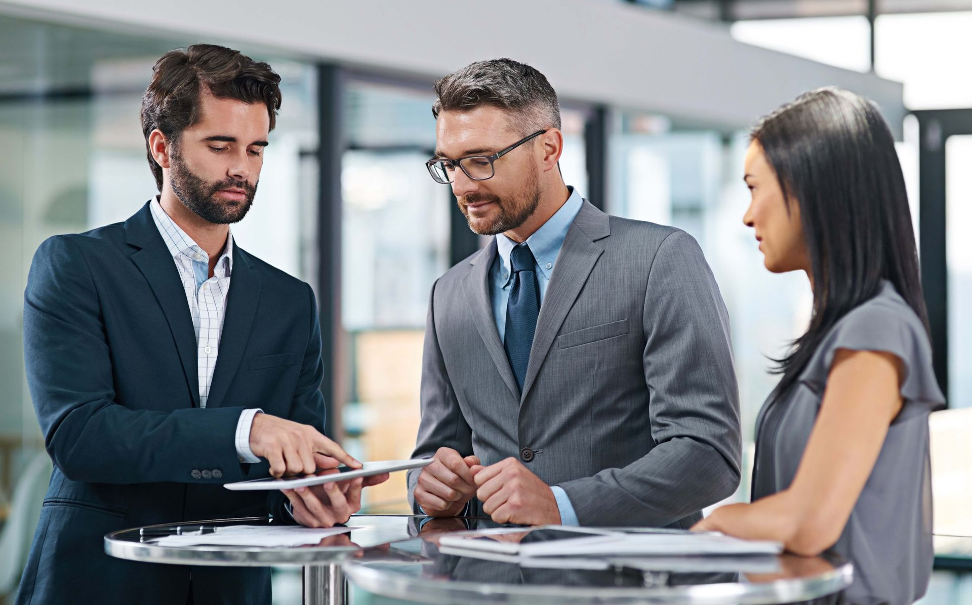 a  group of business people are standing around a table looking at a tablet