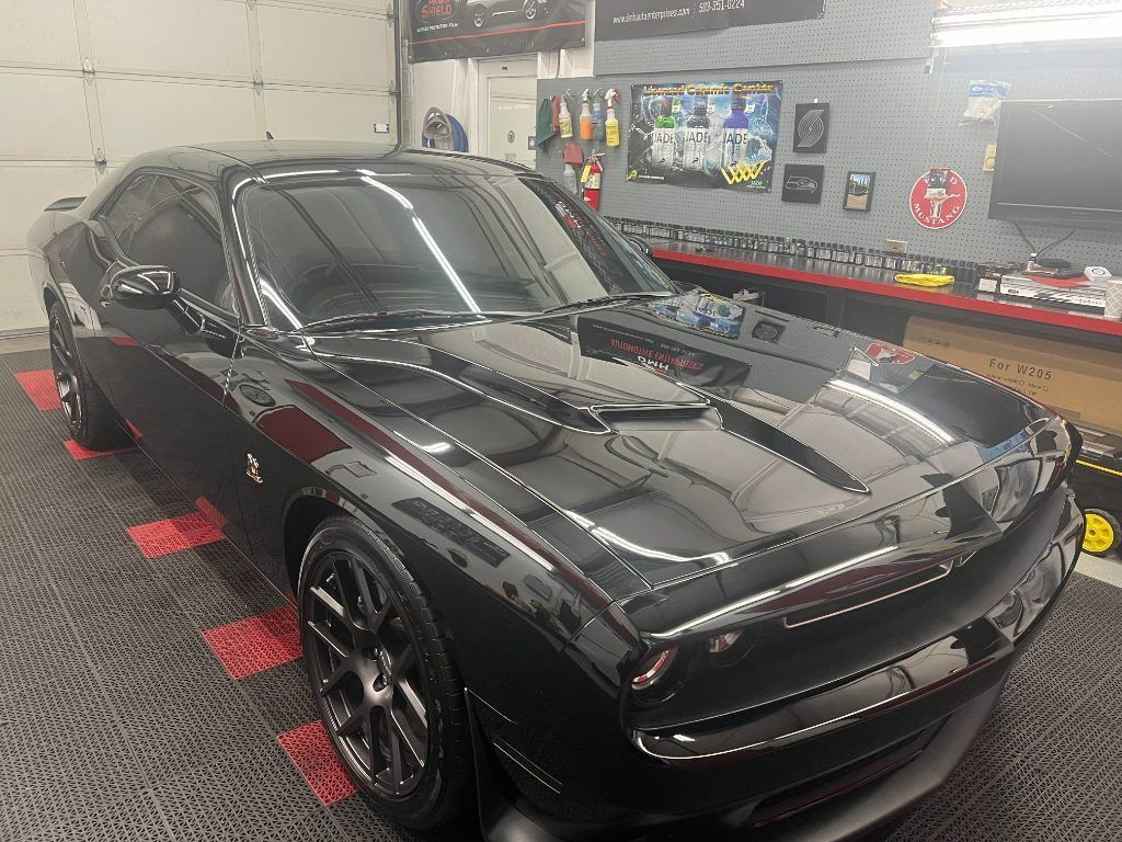 Black sports car in a garage, with glossy reflections and tools on the wall behind it