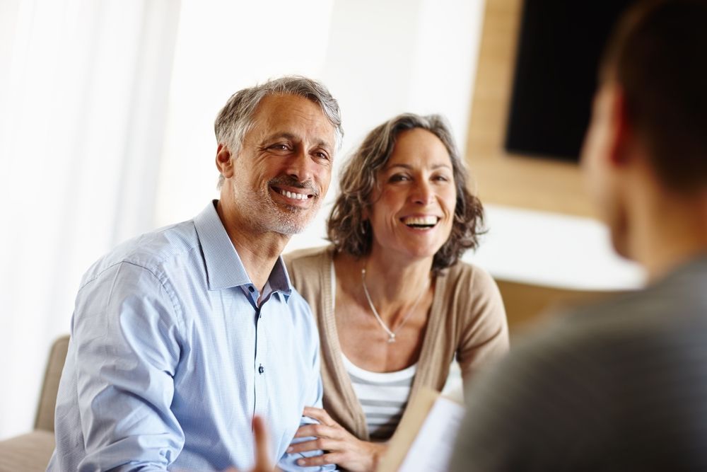 A man and a woman are sitting on a couch talking to a man.