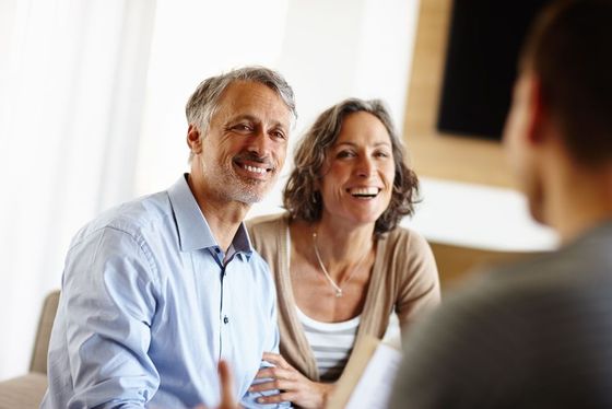 A man and a woman are sitting on a couch talking to a man.