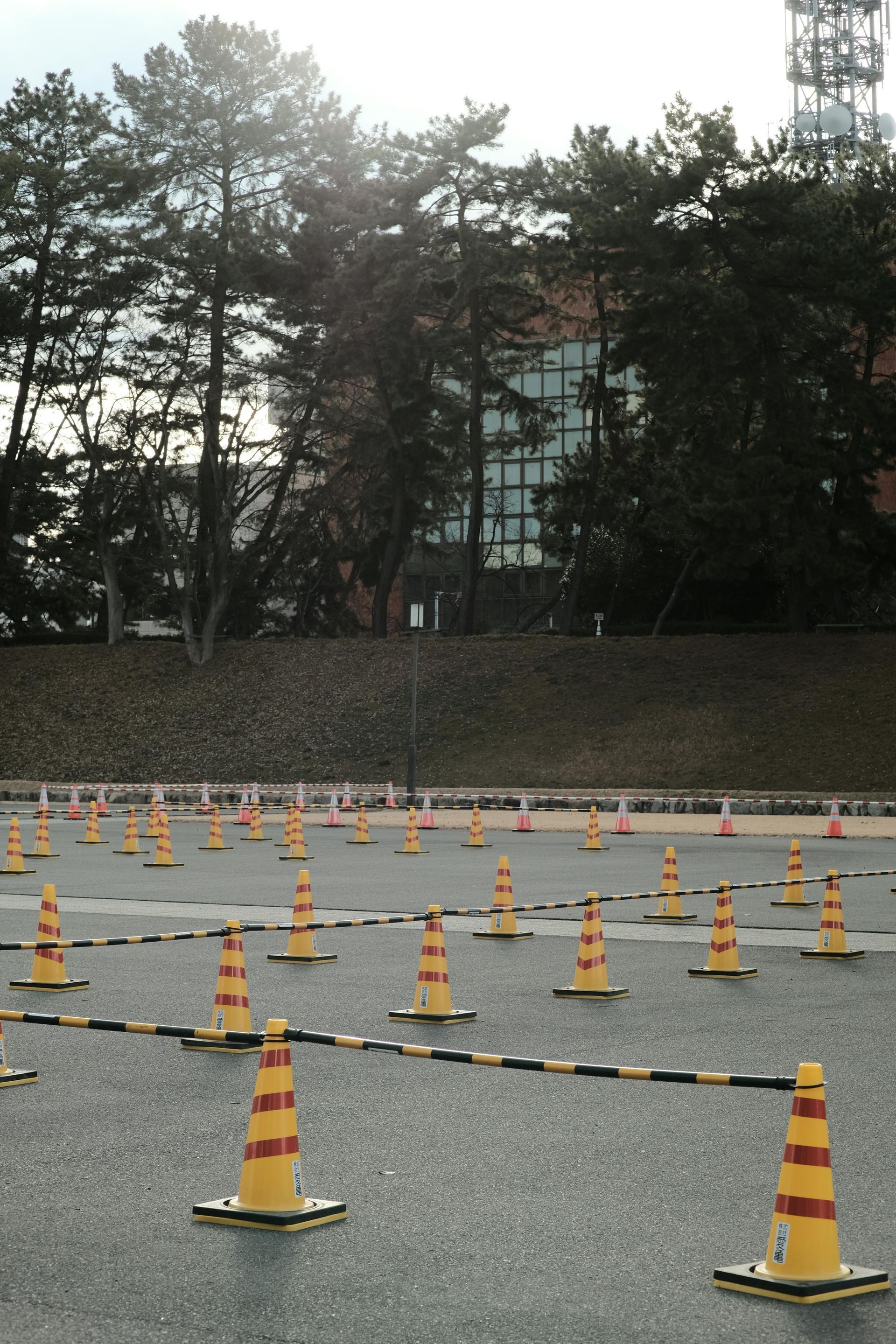 Parking lot with orange and yellow traffic cones and a building in the background.