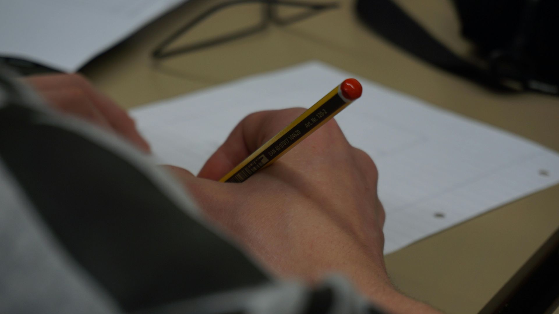 Person writing on a blank white paper with a pencil; close-up view of hands and paper.