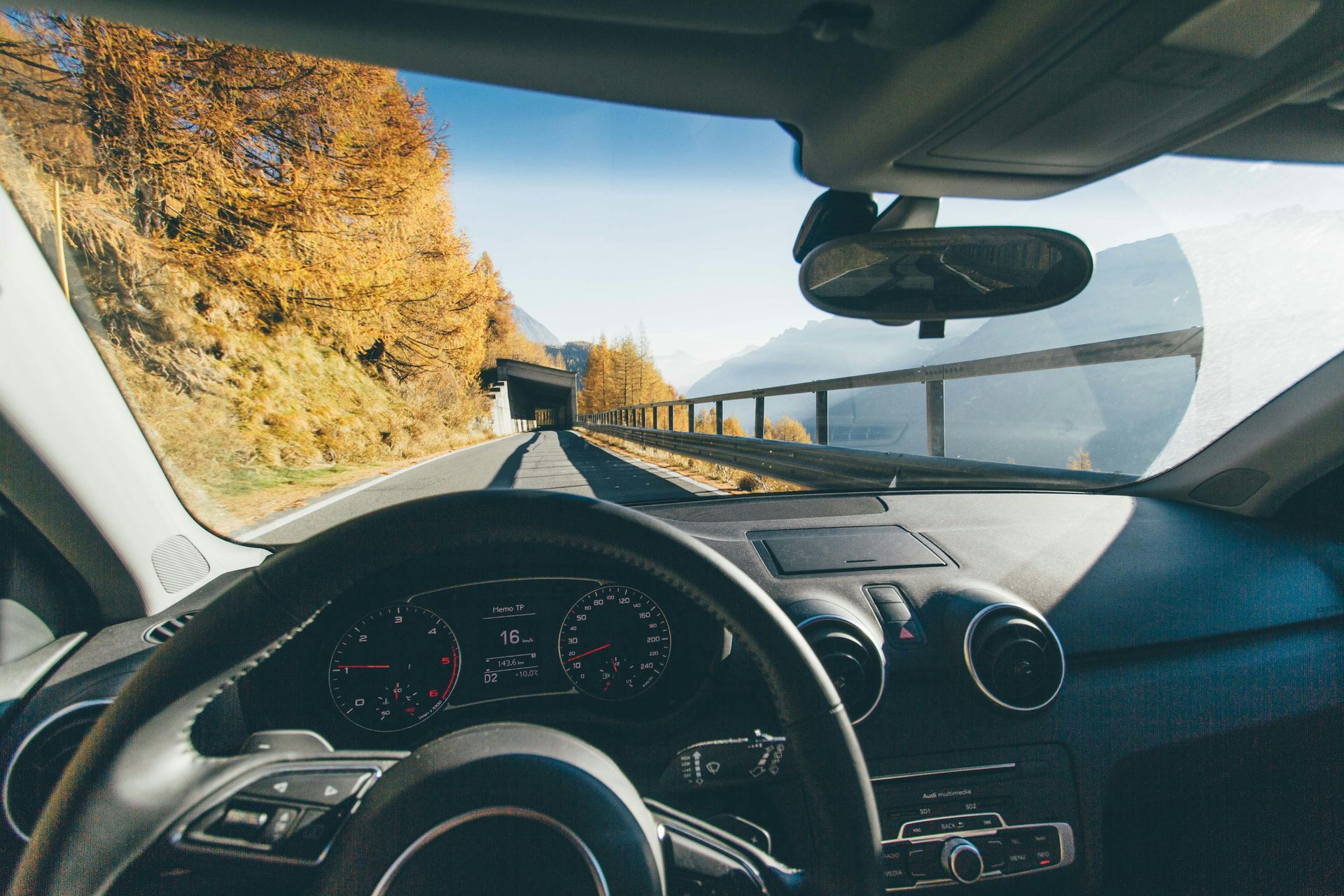 Inside car view driving toward tunnel, fall foliage, sunny day.