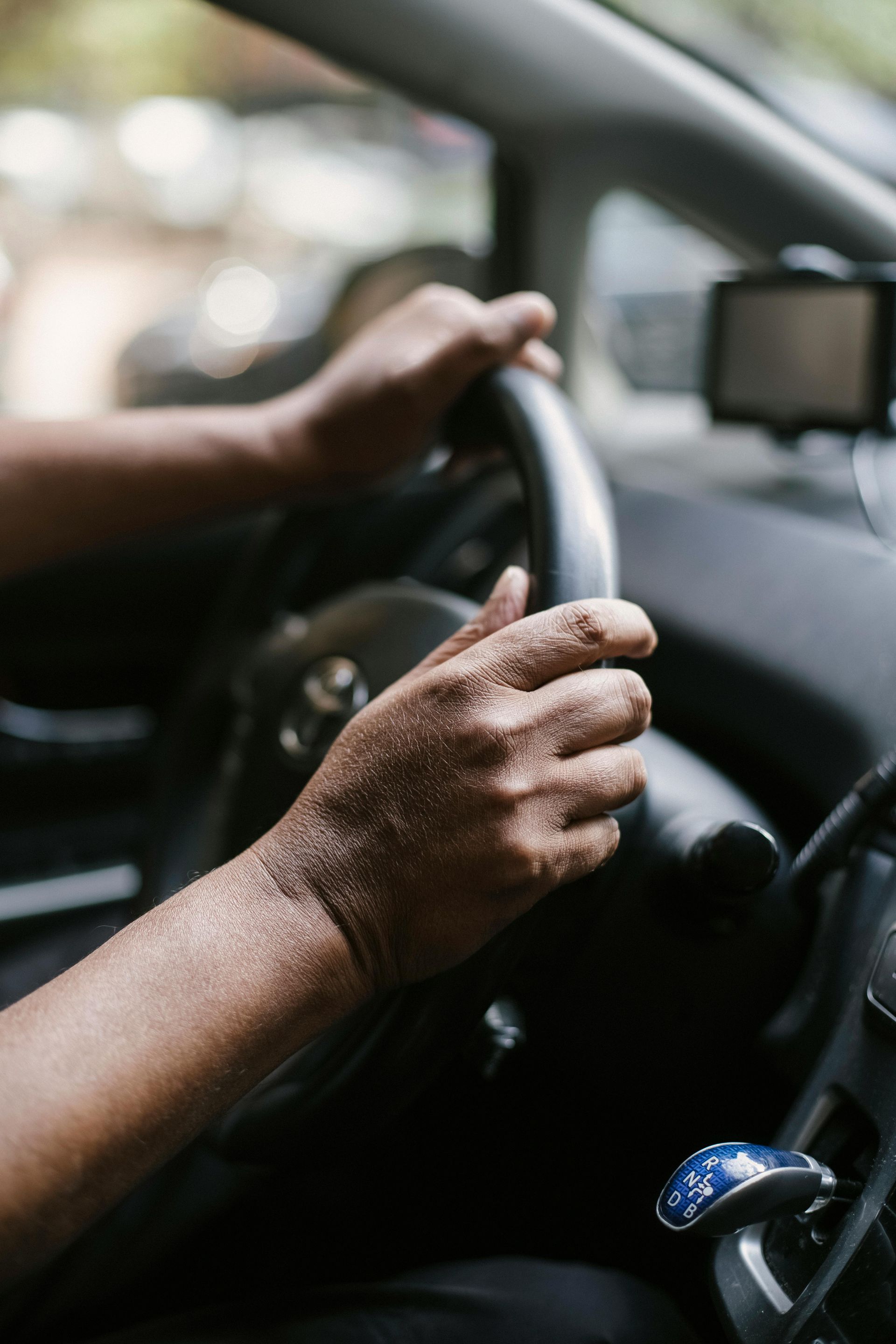 Hands gripping a car steering wheel; interior view.