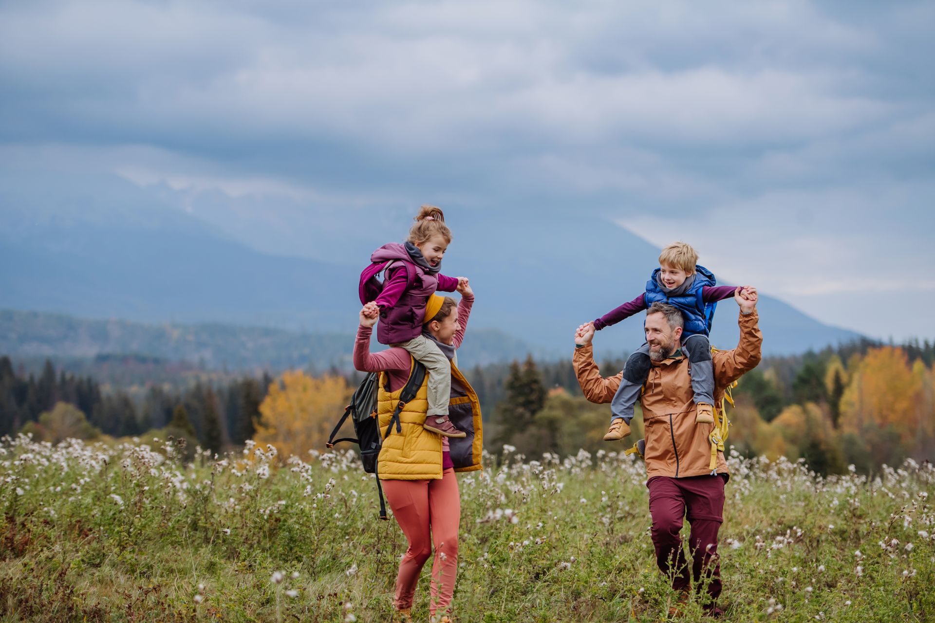 A family is walking through a field with their children on their shoulders.