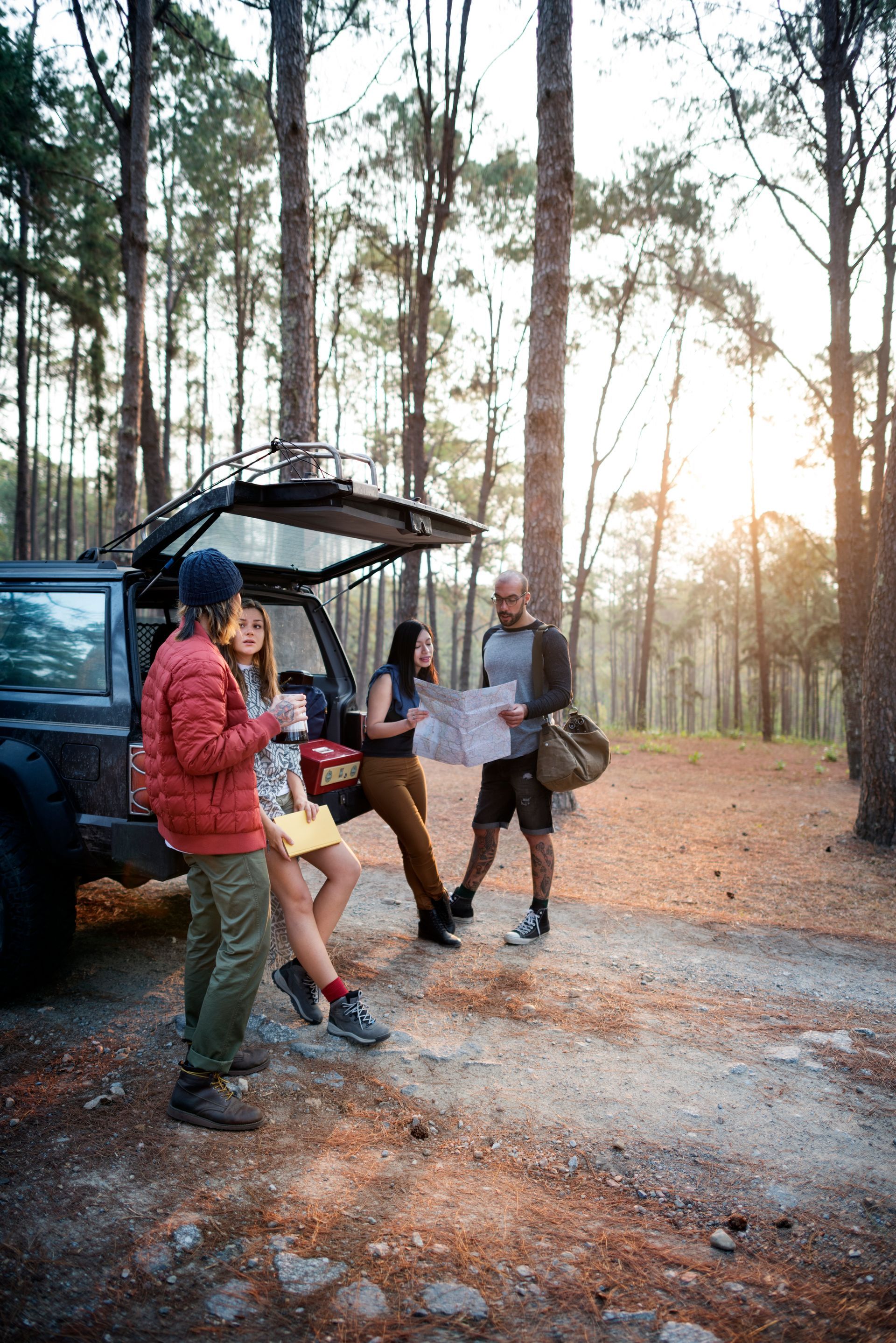 A group of people are standing next to a car in the woods.