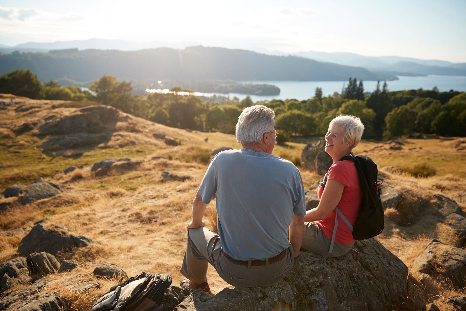 A man and a woman are sitting on a rock overlooking a lake.