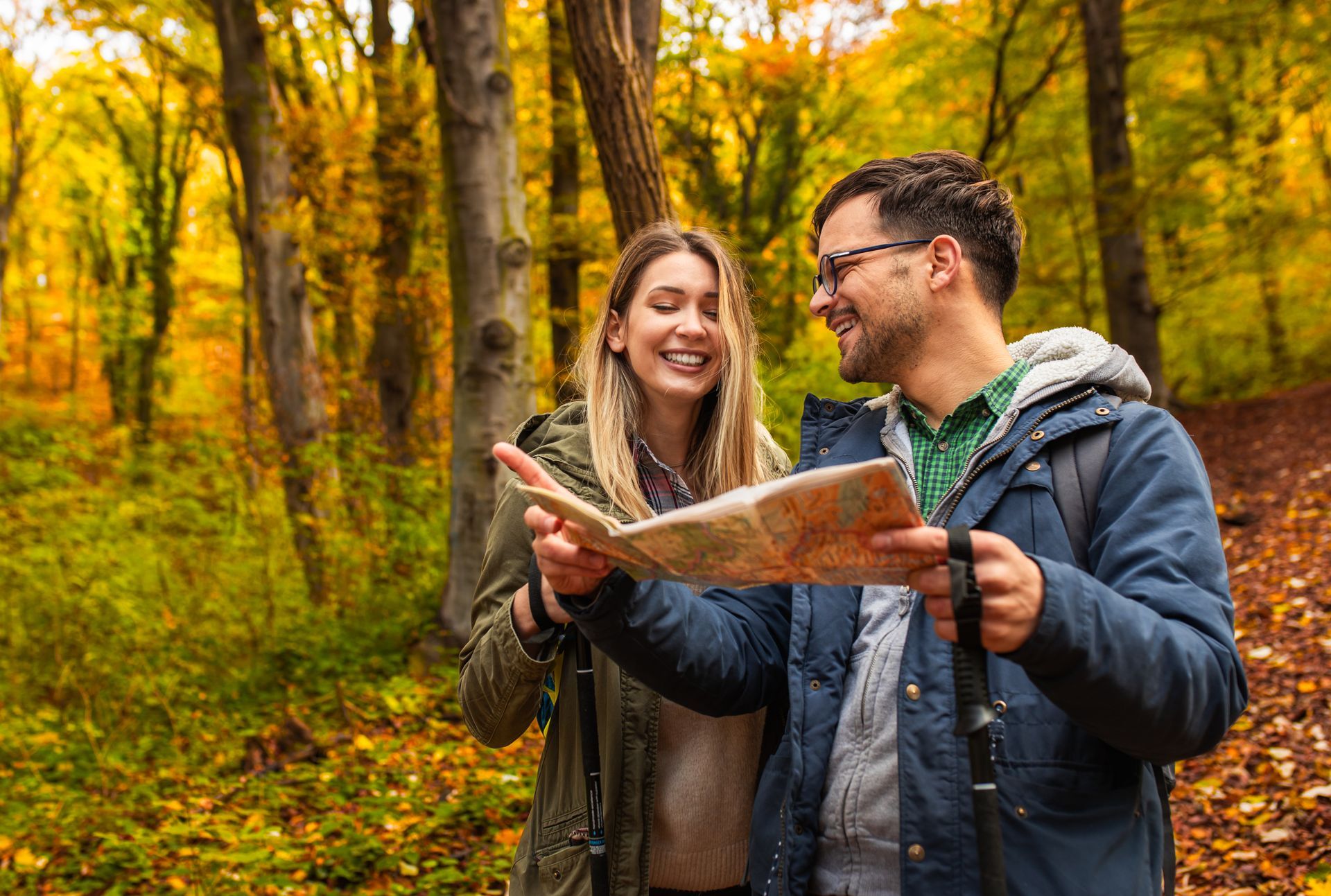 A man and a woman are looking at a map in the woods.