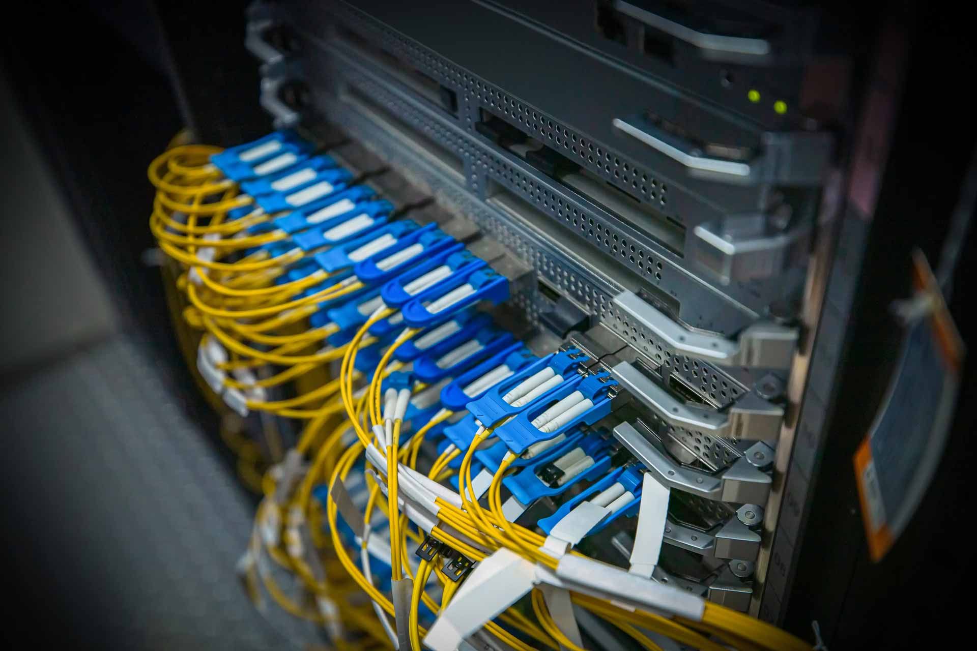 Server rack with blue and yellow fiber optic cables plugged in.