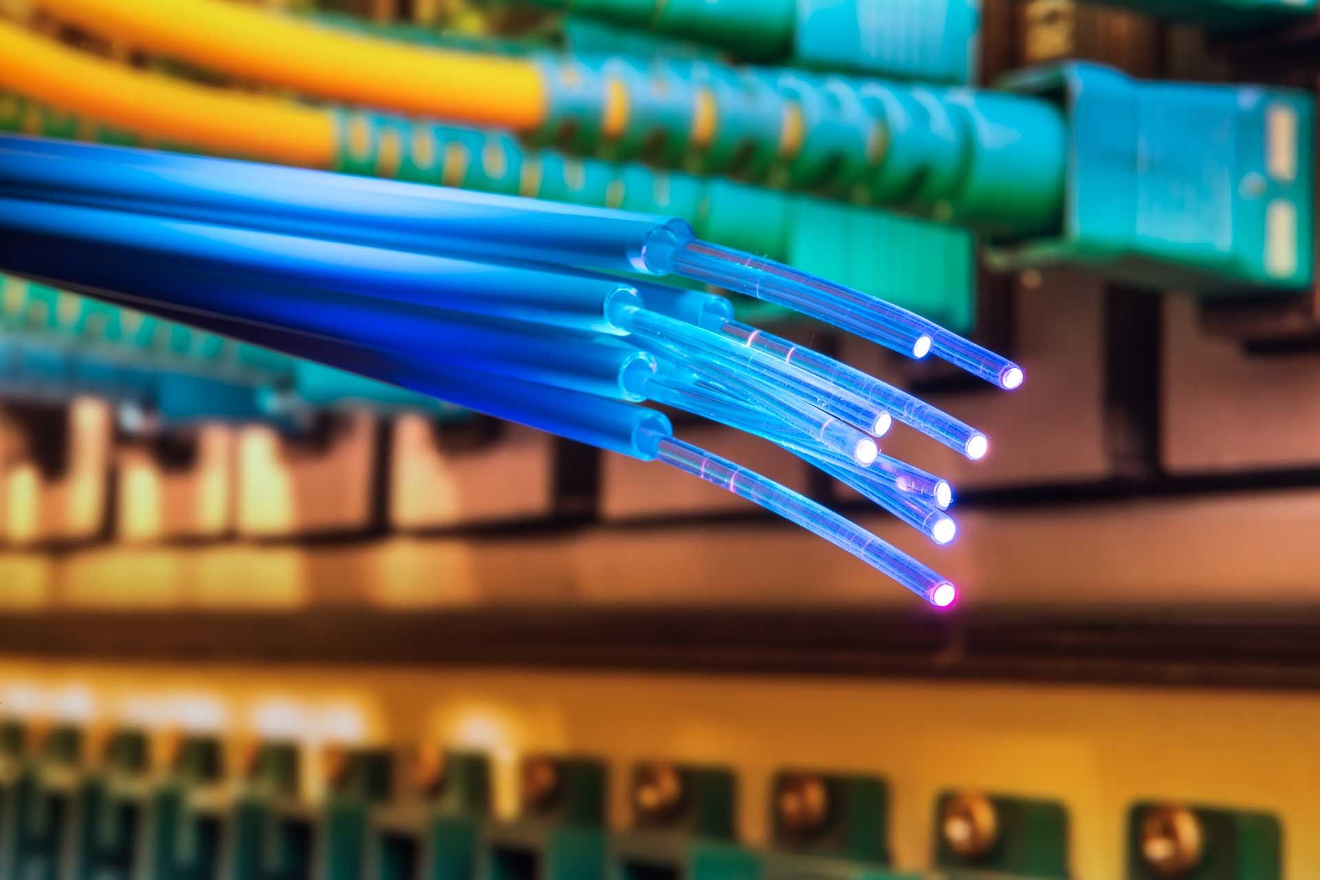 Blue fiber optic cables emitting light, plugged into a green server