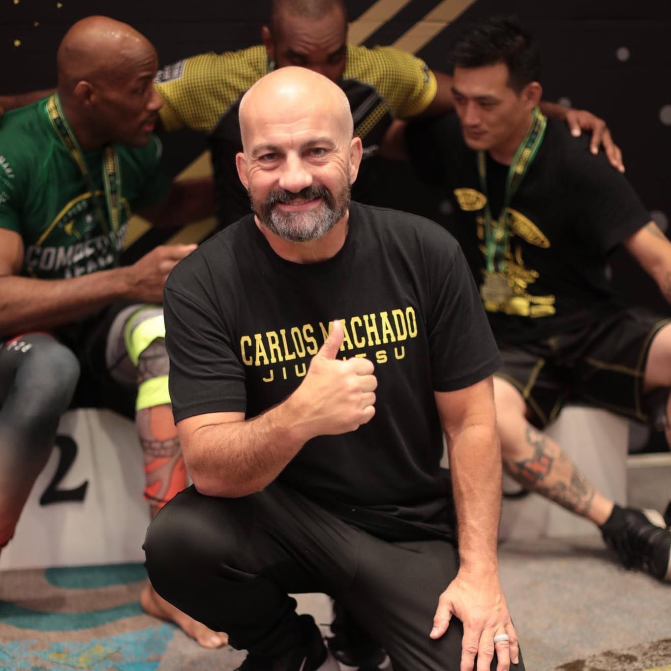A man wearing a carlos machado shirt gives a thumbs up