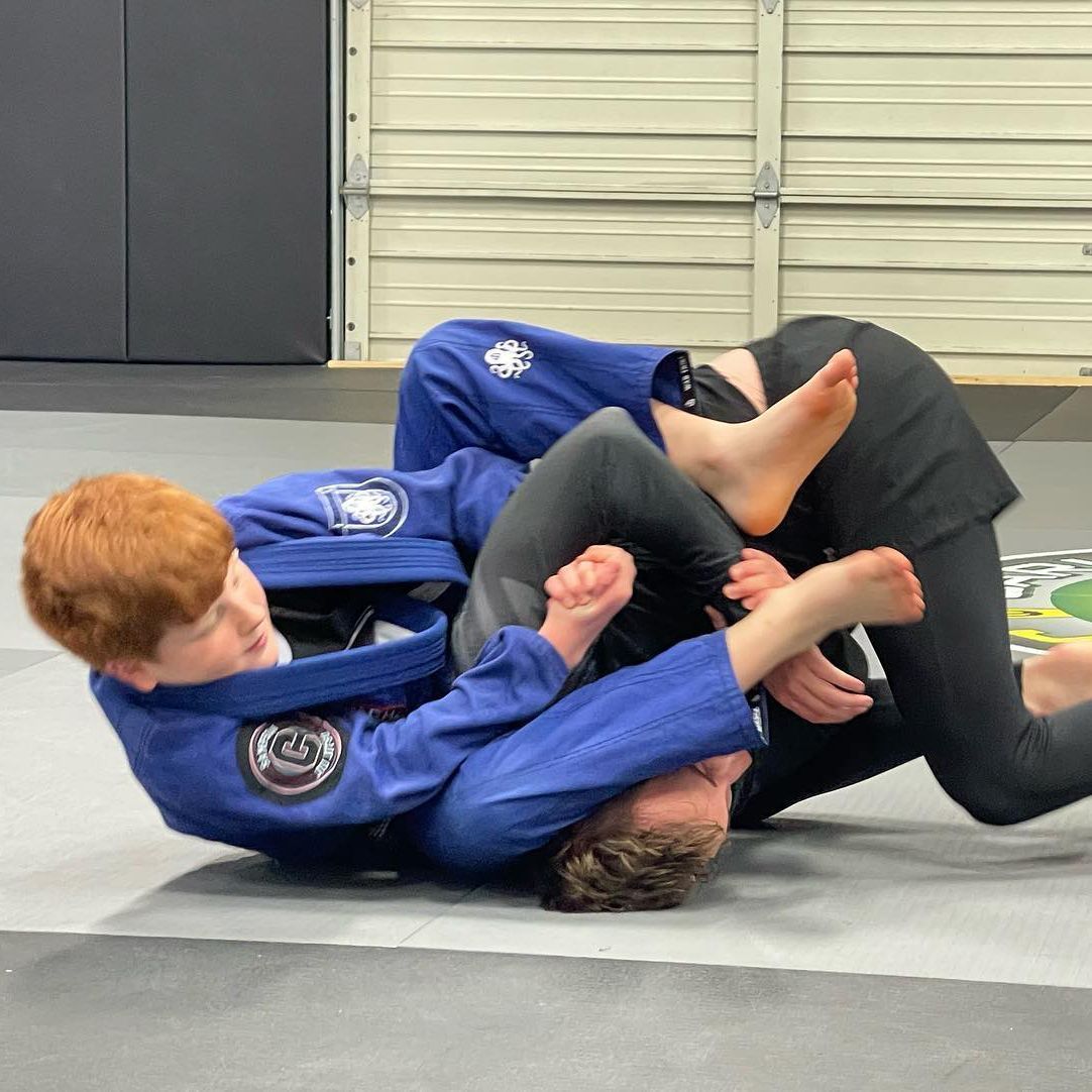 Two boys are wrestling on a mat in a gym