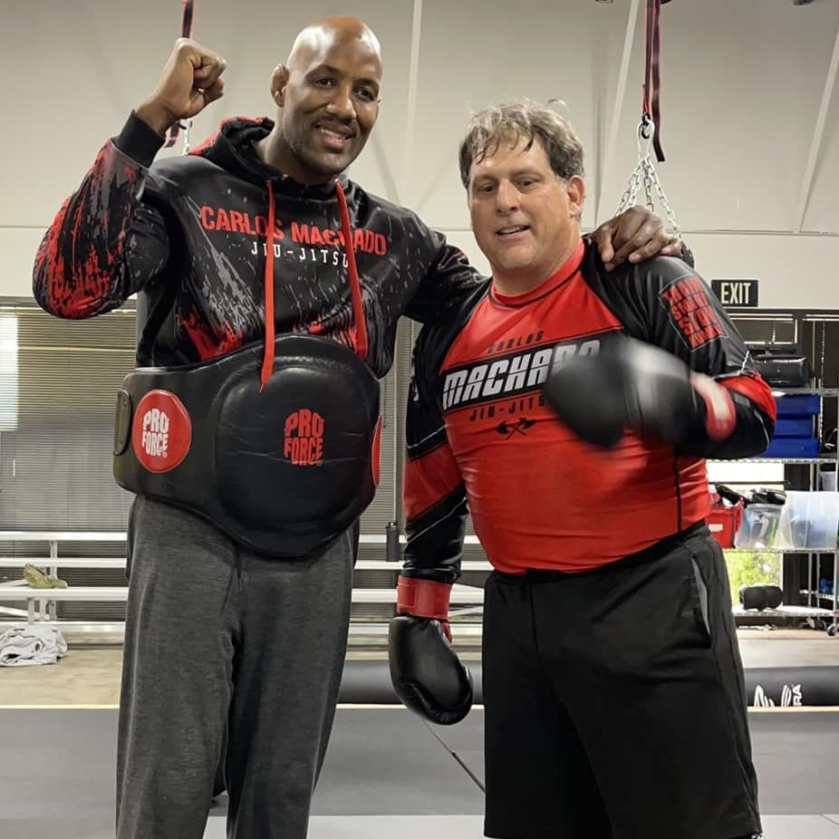 Two men are posing for a picture in a boxing ring and one of them is wearing boxing gloves