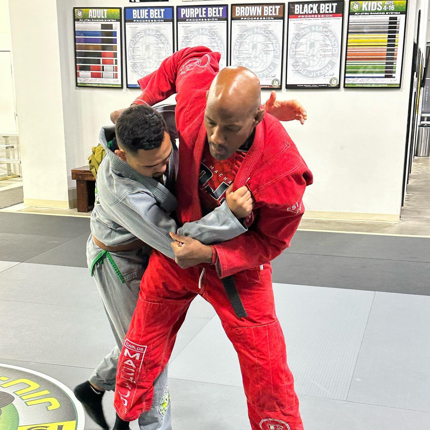 Two men are wrestling on a mat in a gym.