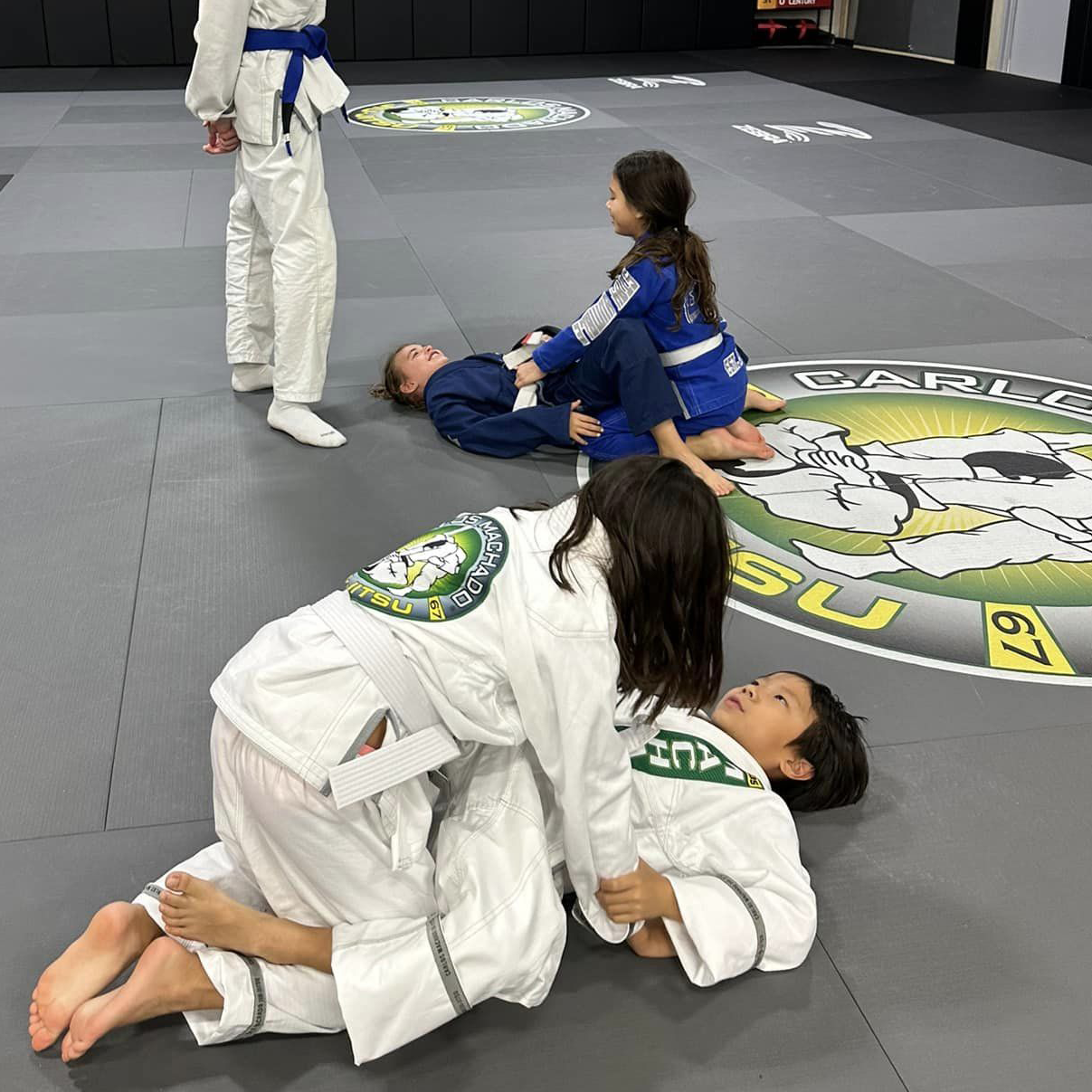 A group of children are practicing martial arts on a mat in a gym.