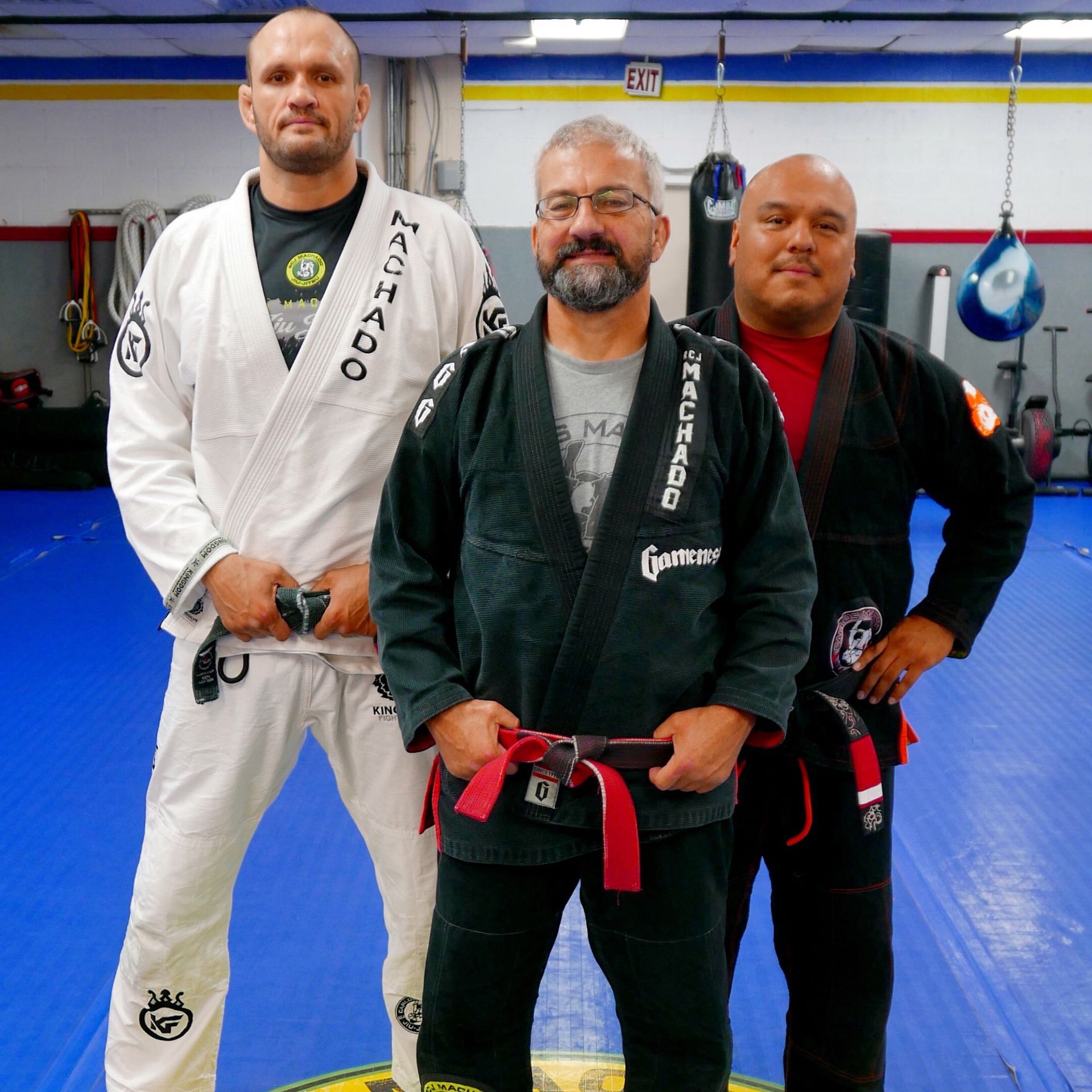 Three men are posing for a picture in a gym with one wearing a karate uniform