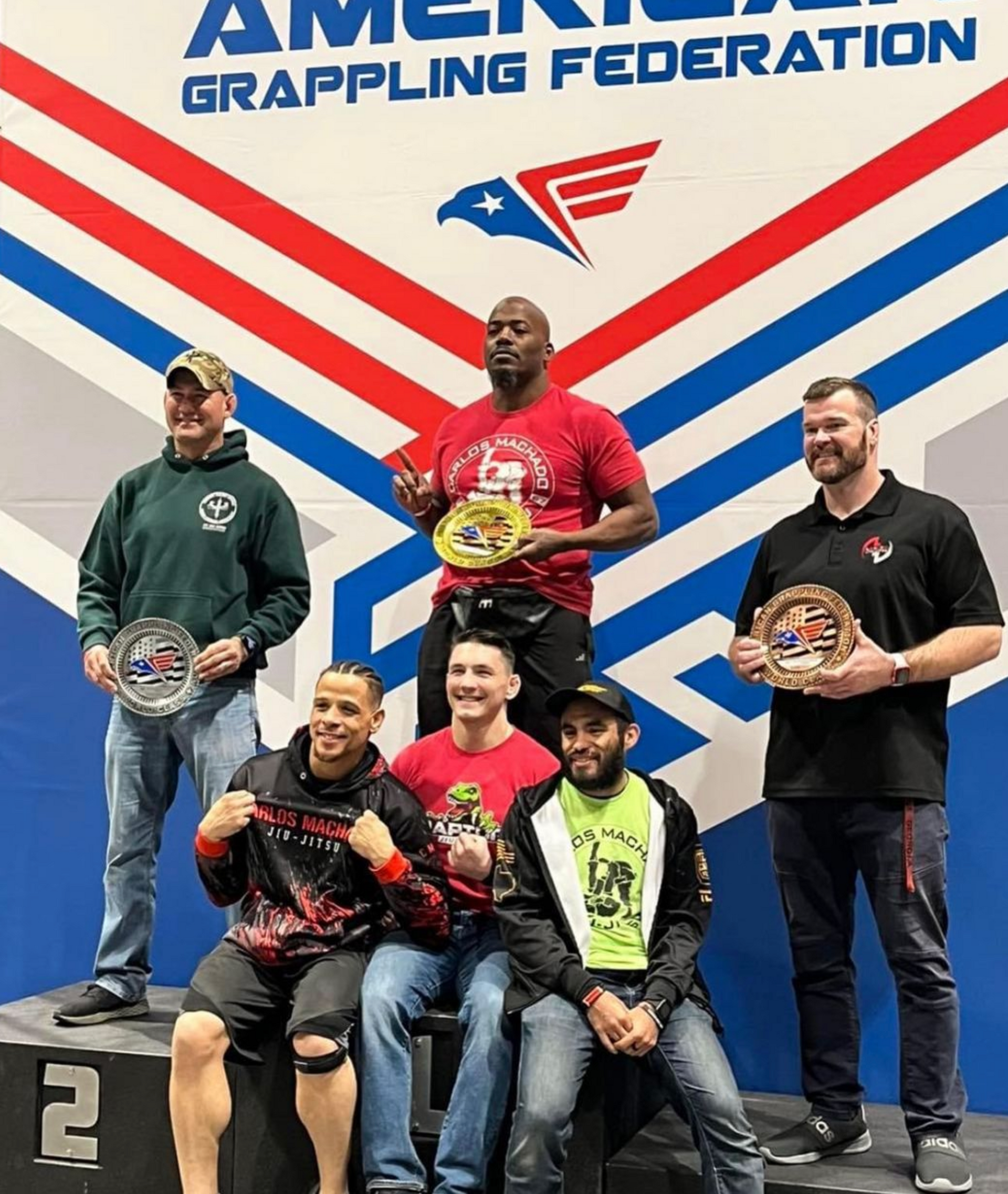 A group of men are standing on a podium in front of a wall that says american grappling federation