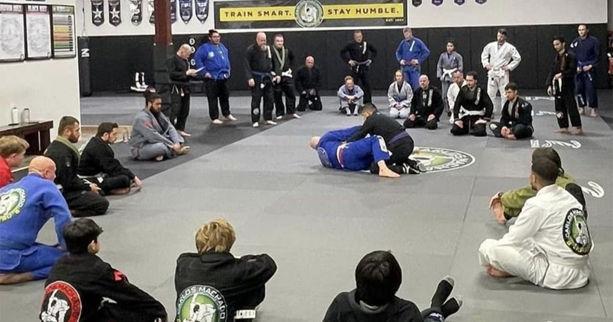 a group of people are sitting on the floor in a gym watching a karate match.
