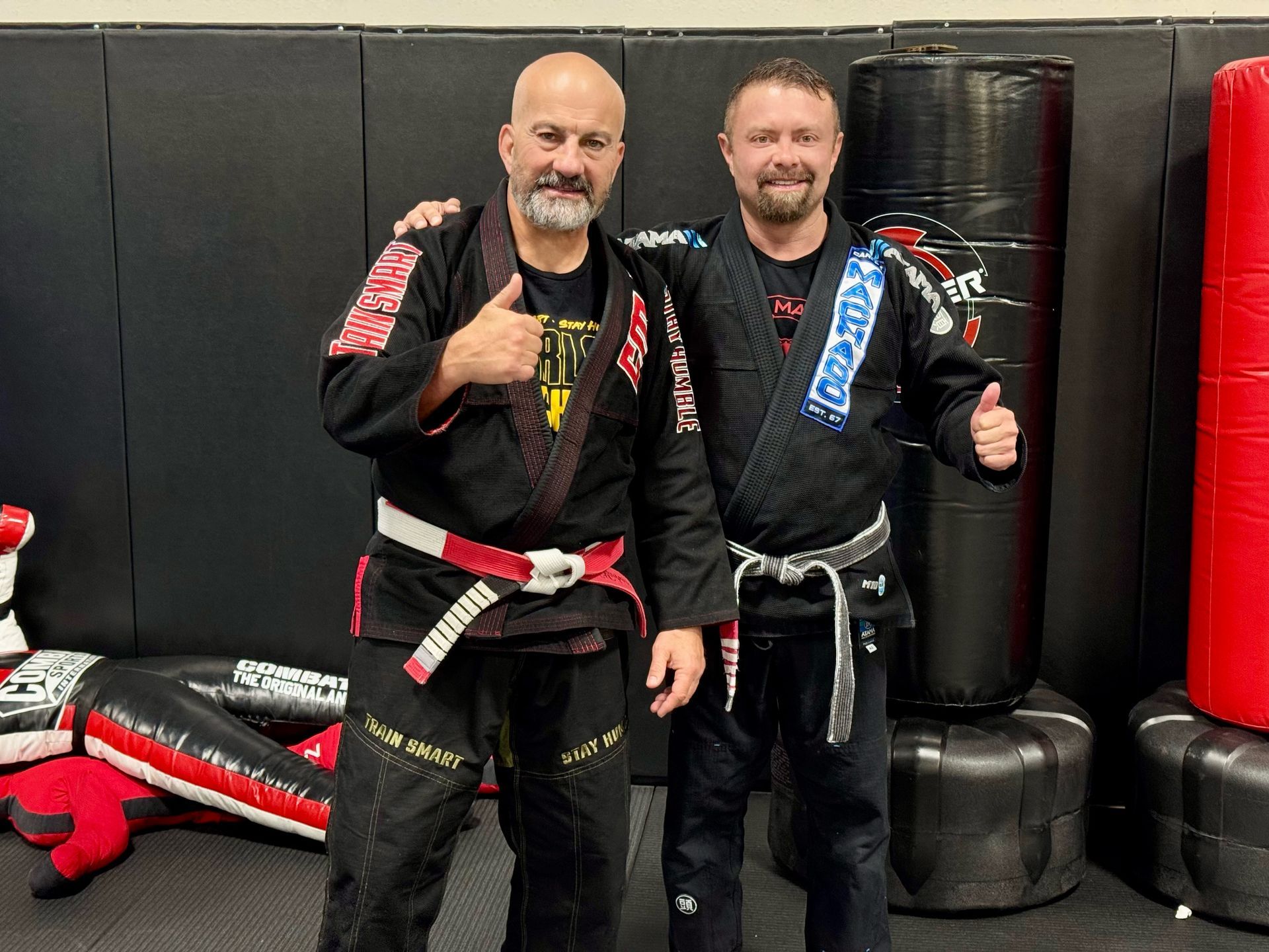 Two men in karate uniforms are posing for a picture in a gym.