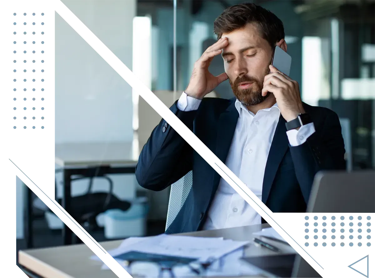 A man in a suit is sitting at a desk talking on a cell phone.